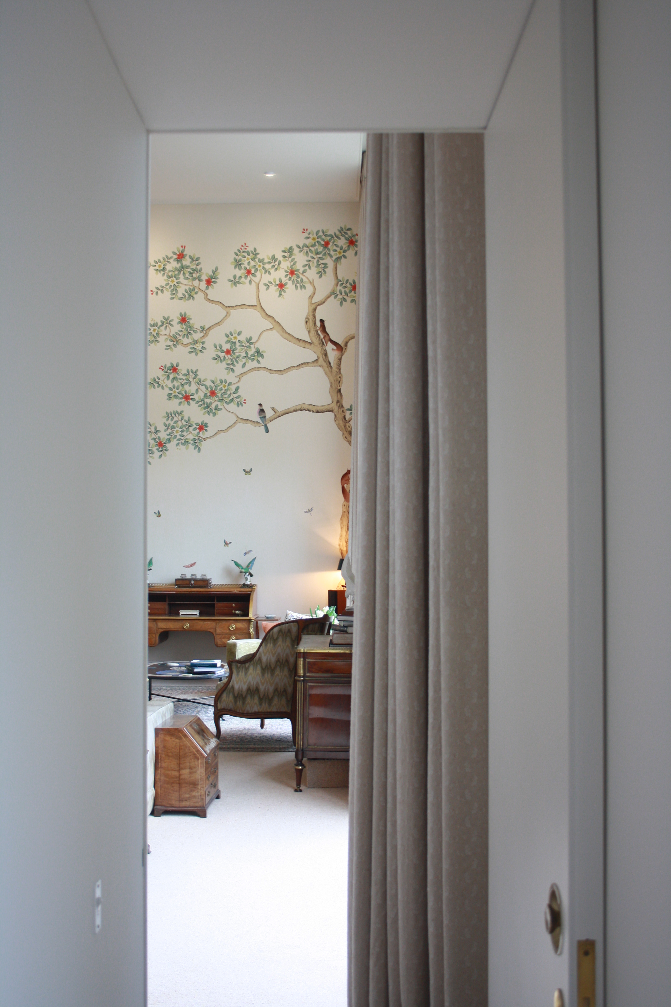 Long Serge neutral curtains frame the entrance to the formal living room, featuring a bespoke hand painted and hand embroidered mural
