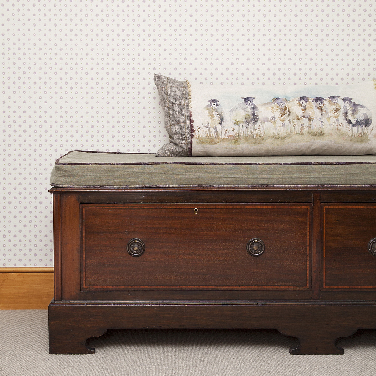 An old low chest with the addition of a soft moss green linen seat cushion with contrast piping.