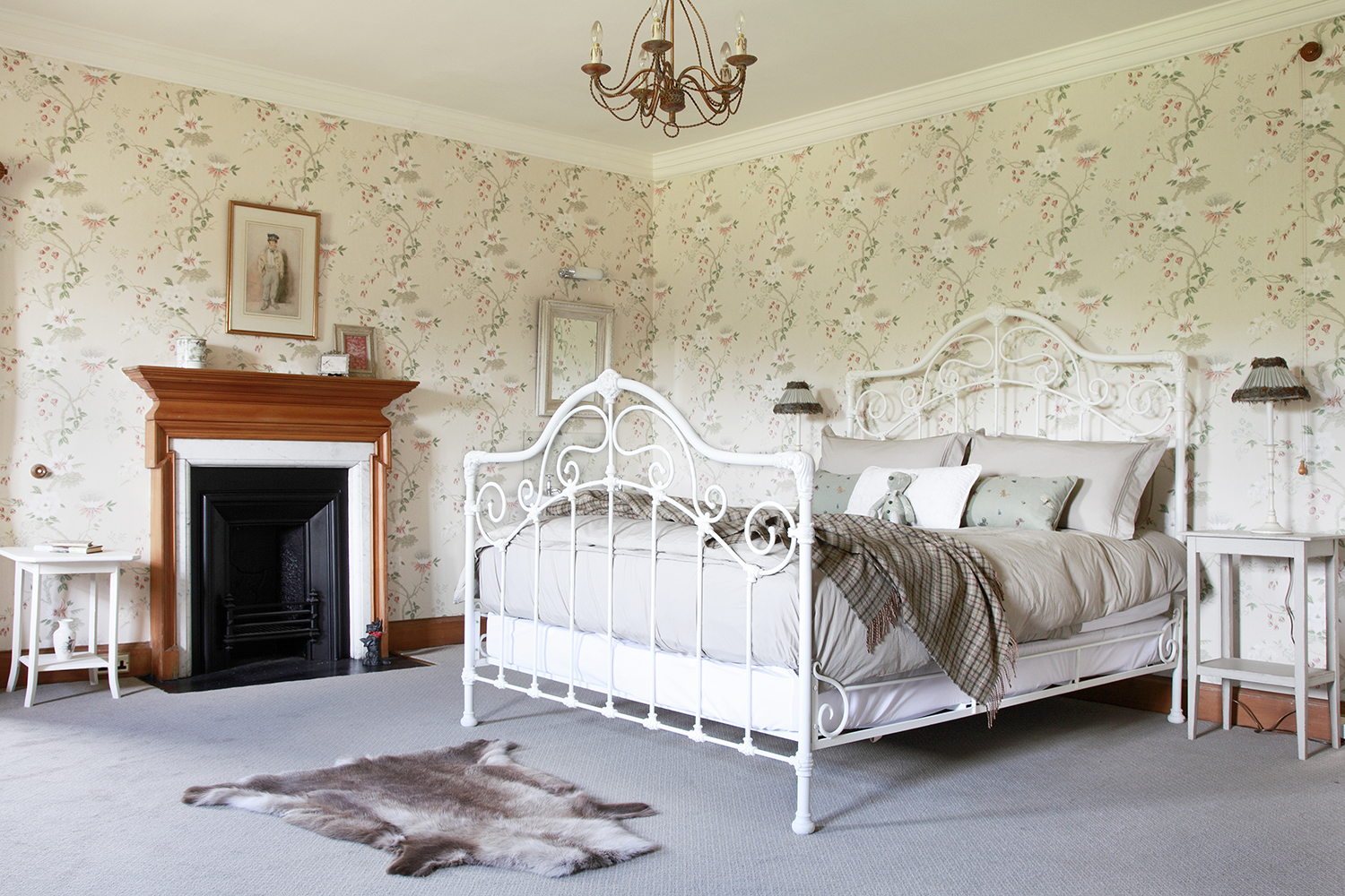 A vintage style cream ironwork bedstead with gentle swirls of passion flowers and buds decorating the wallpaper.