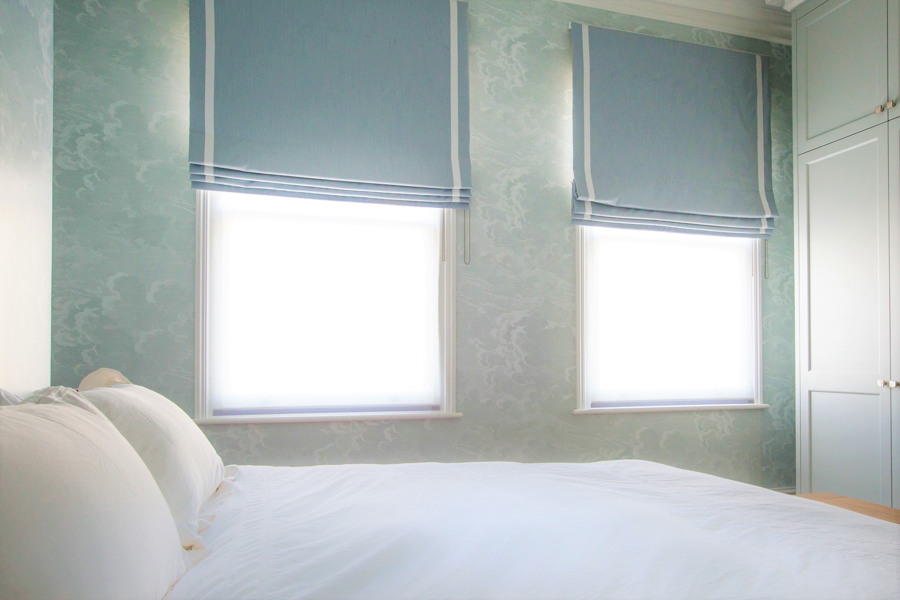 A dreamy and peaceful guest bedroom; cloud patterned wallpaper of heavenly blues ties in with the blue roman blinds