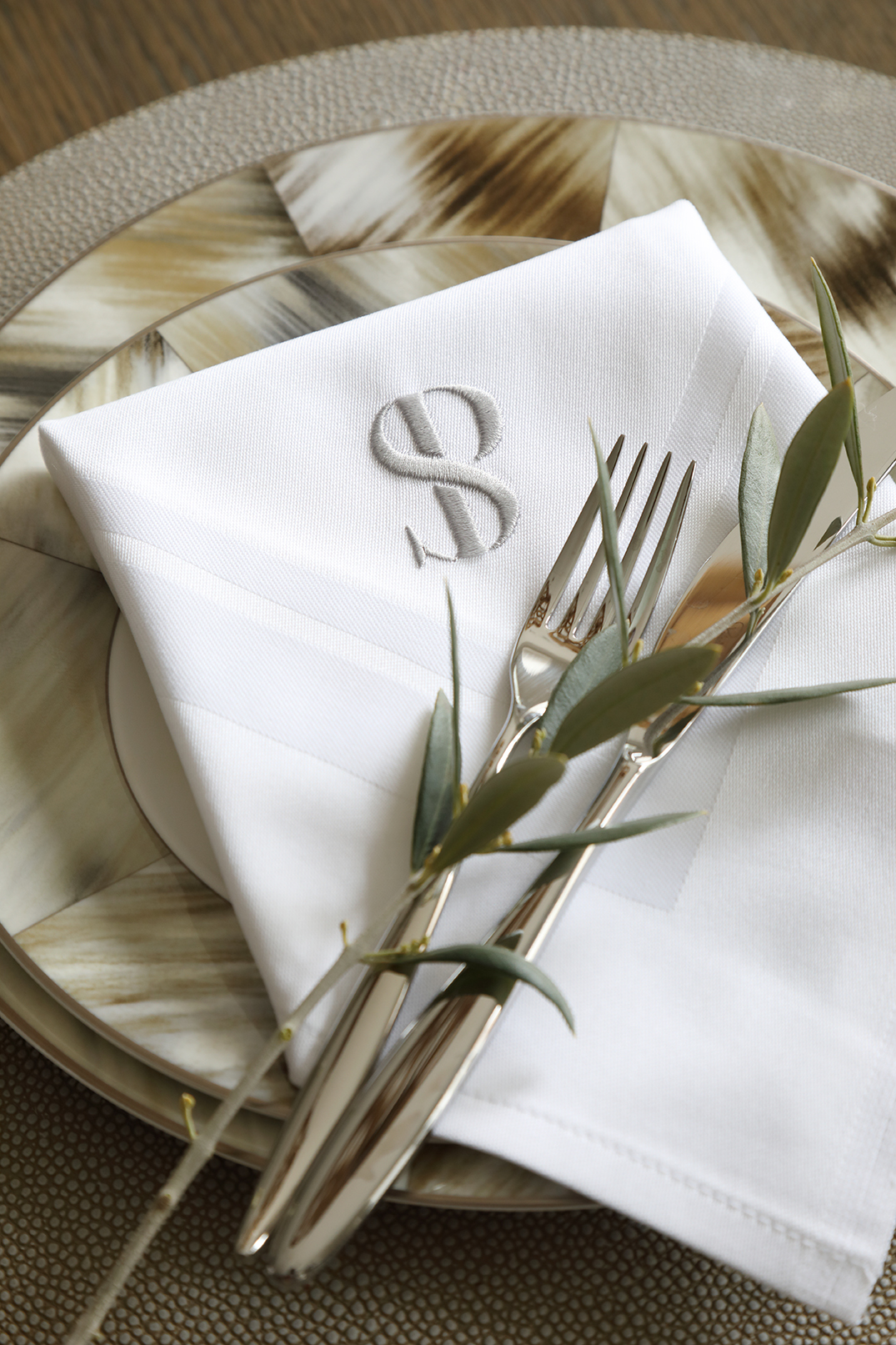 Monogrammed napkin on a patterned plate with fork and olive twig