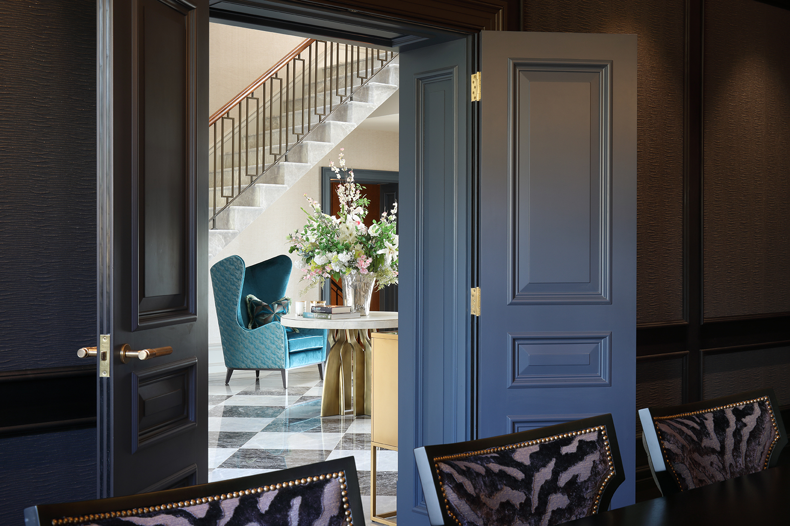 View from dining room through double doors to hall with turquoise wingback chair and staircase