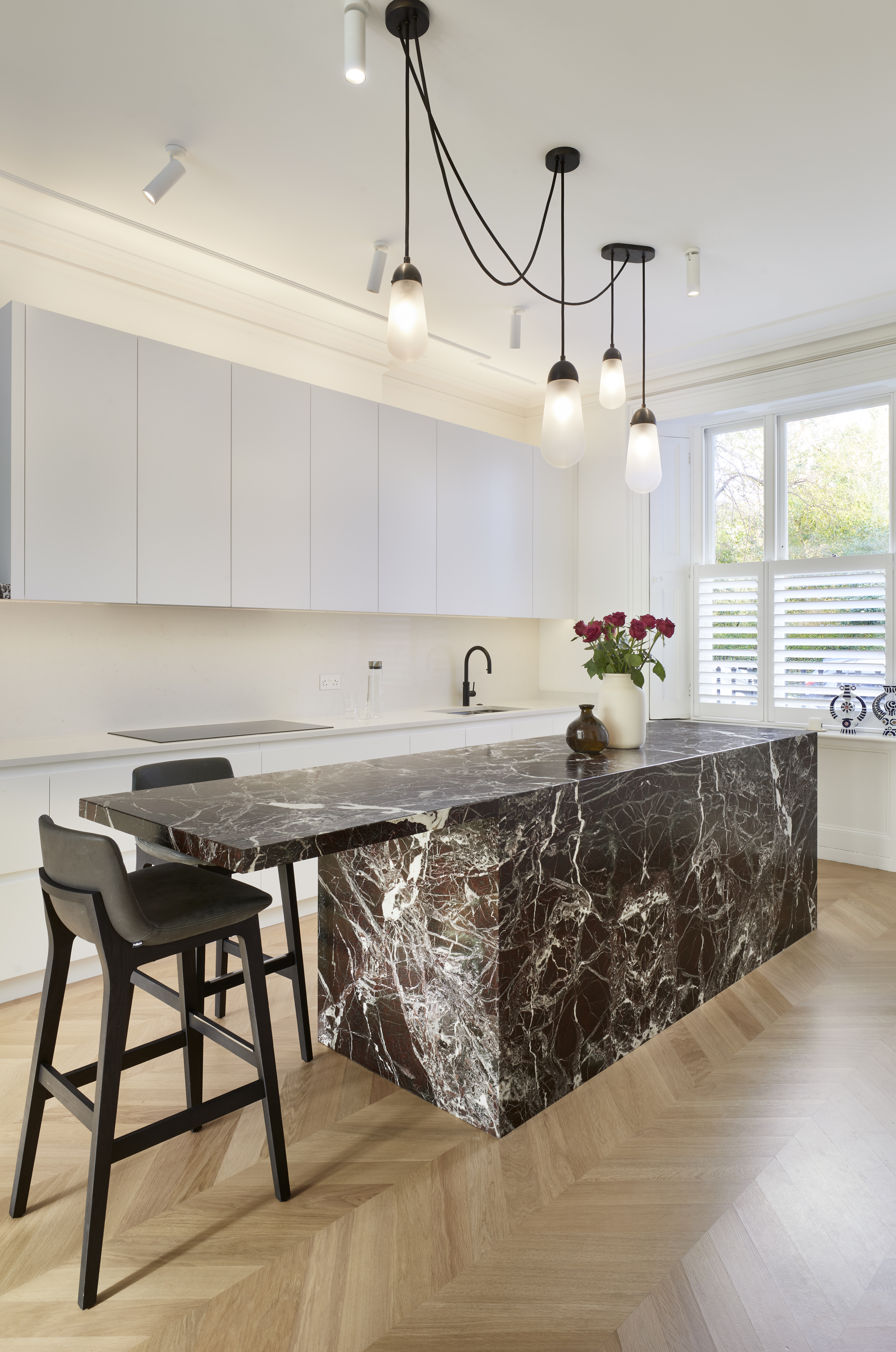 An angled view of a marble clad kitchen island with bar stools & white painted cabinets