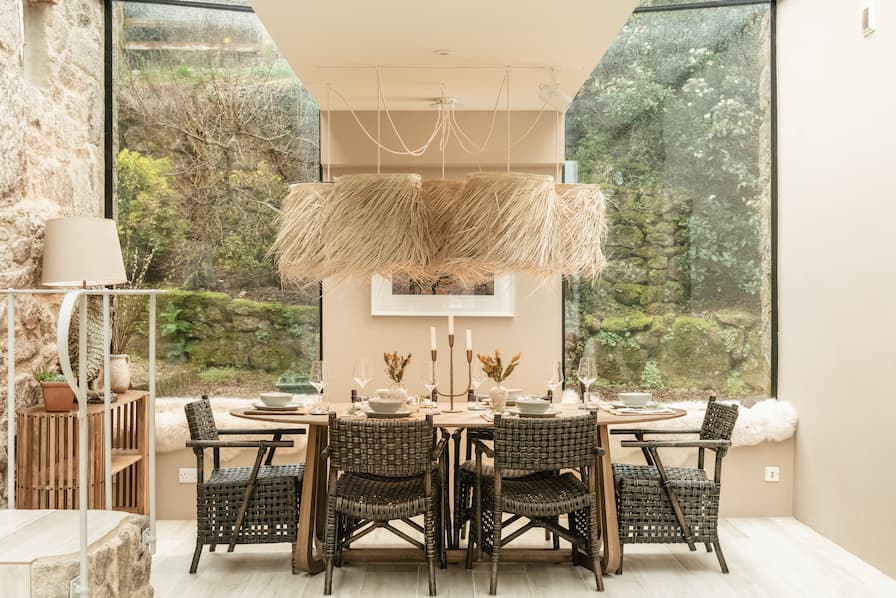 Raffia shades hang over a solid wood dining table, with rattan chairs