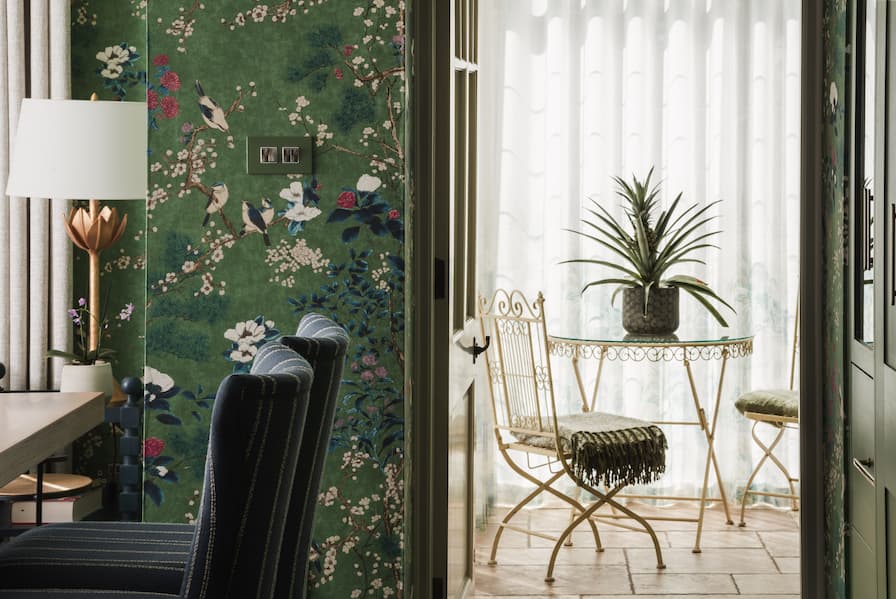 Looking through doorway from wallpapered Kitchen to bright Garden Room, filled with plants