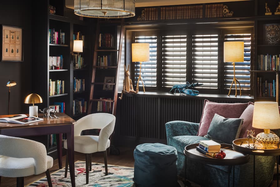 Dark and moody library filled with books, with snuggly love seat chair and puzzle table