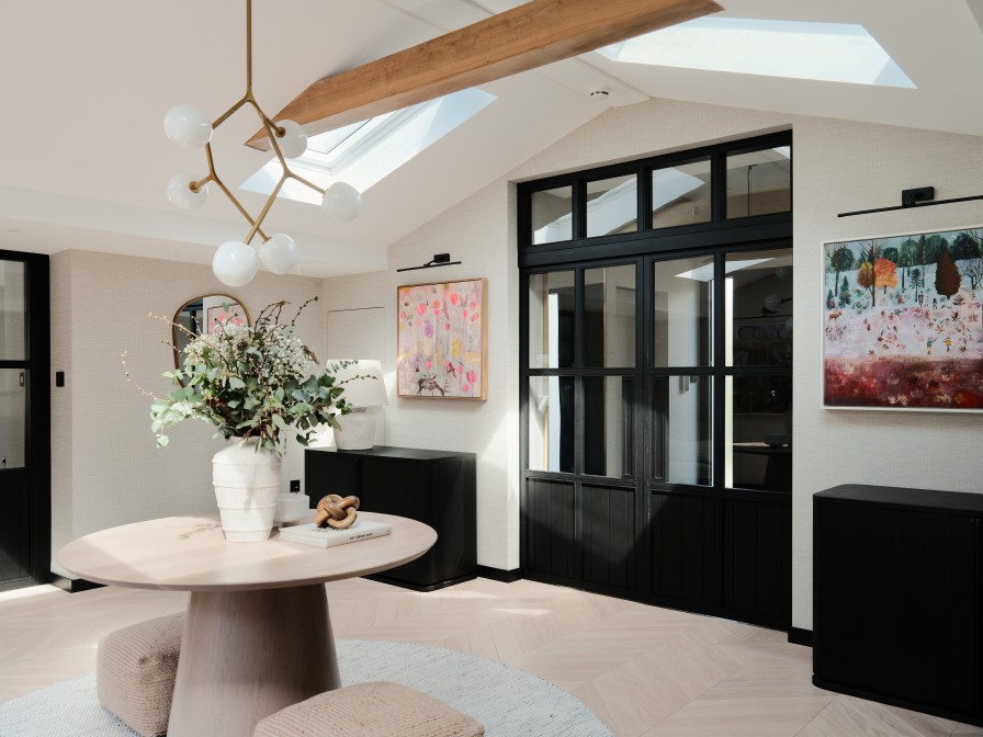 Entrance hall with black crital style doors. Round table in the centre with floral arrangement on top and hanging light above.