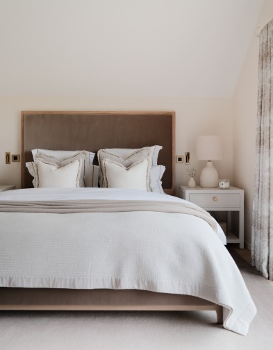 Bed with neutral bedding layered on top. Light oak bed frame with velvet headboard and footboard. 