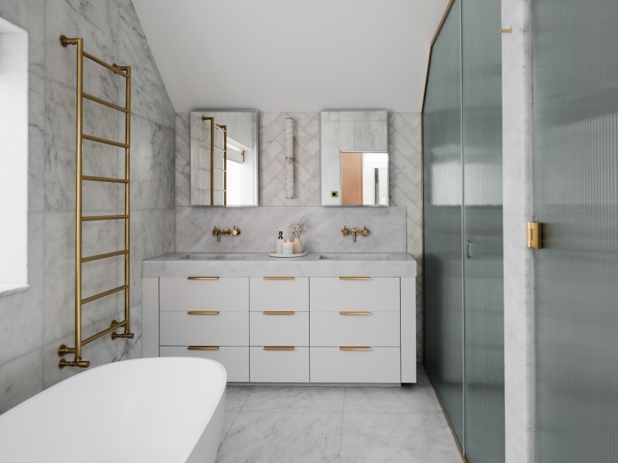 Marble bathroom showing the vanity unit which is white with gold hardware. Mirror cabinet sat above the basins.