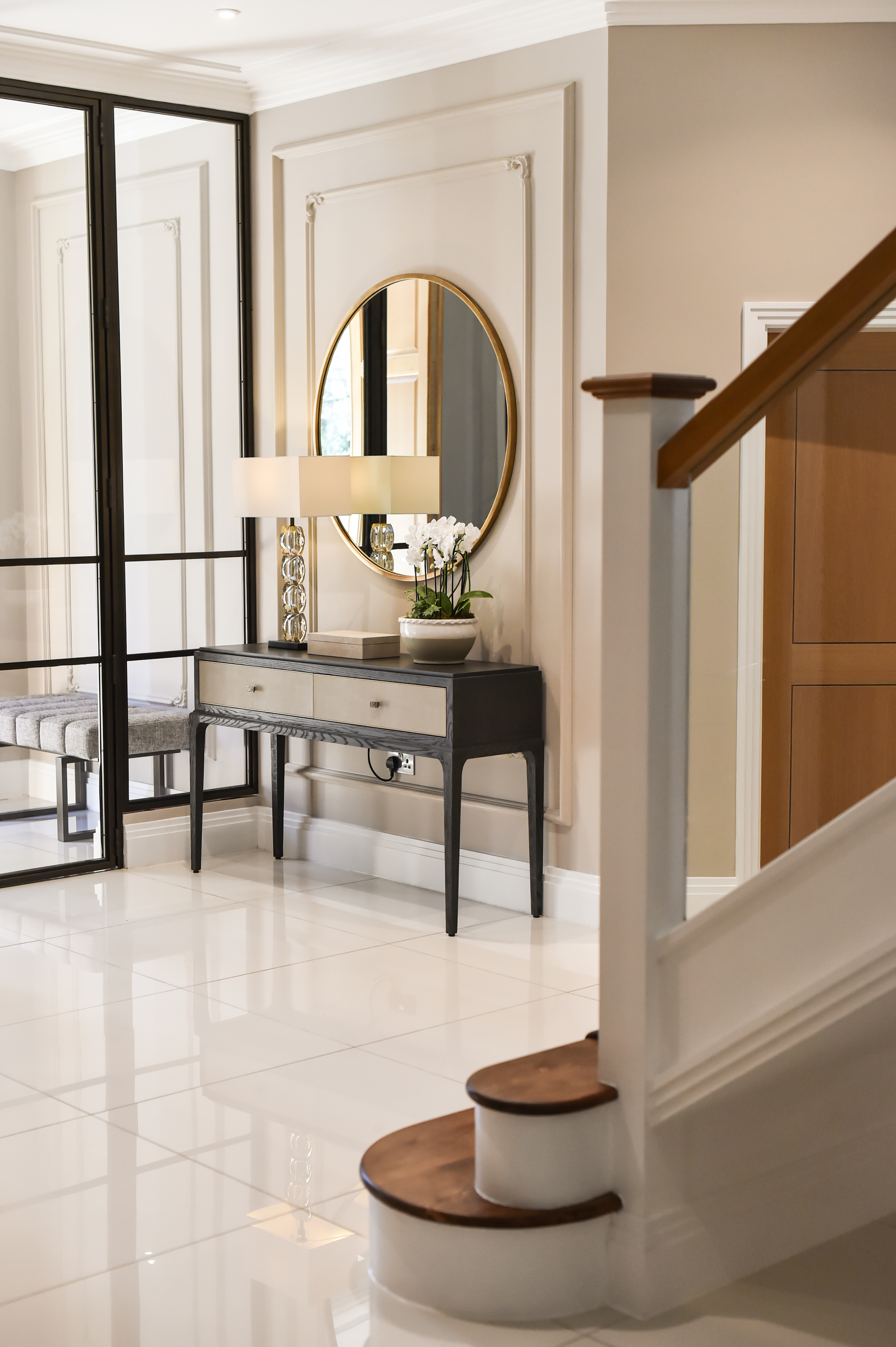Matching console tables with circular mirrors create a harmonious symmetry and double wall moulding with intricate corner details adds depth and a classic touch of sophistication.