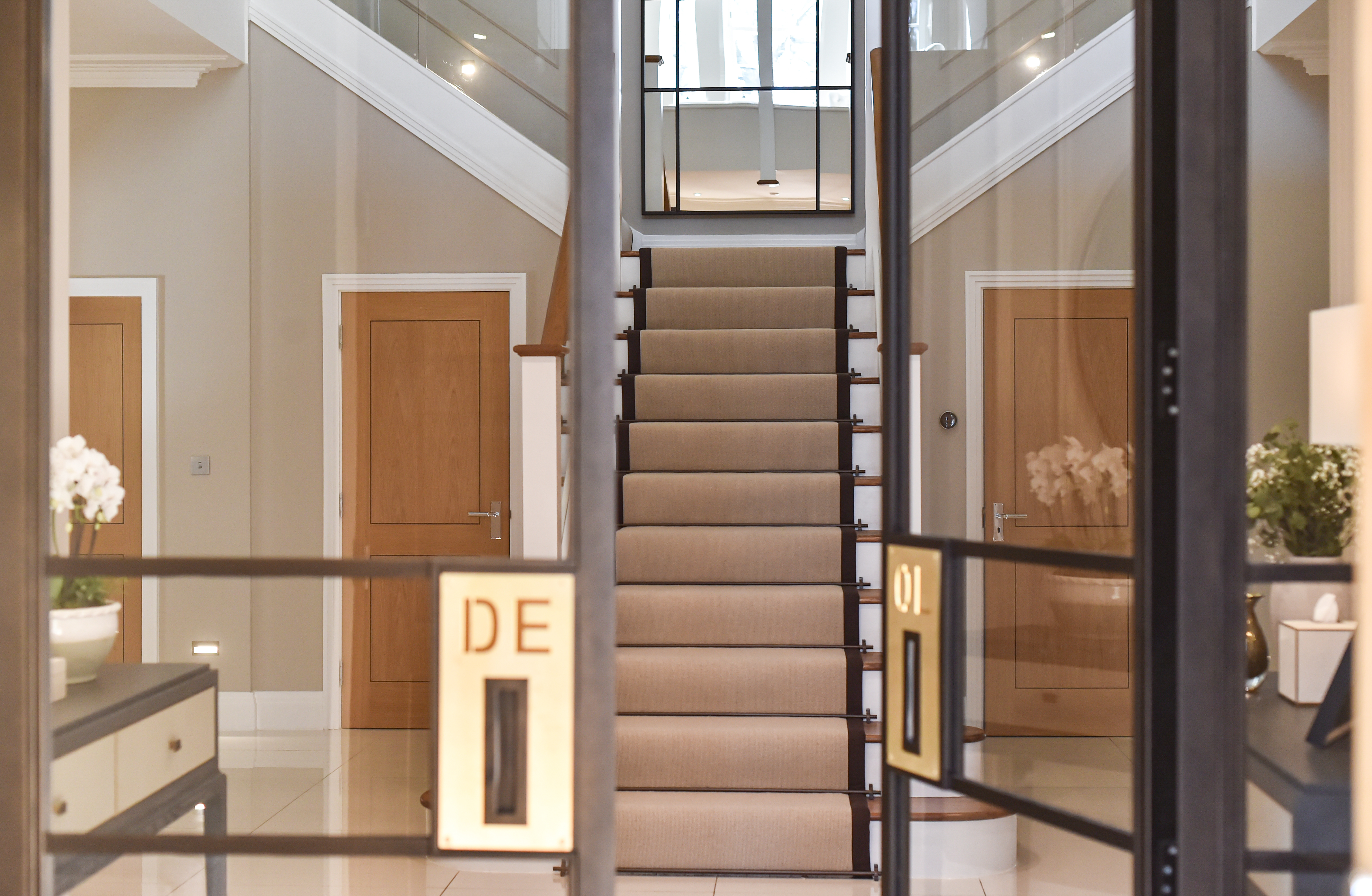 Hallway entrance floor-to-ceiling bespoke metal door in a rich, dark bronze finish. Its brushed brass handles with client's initials, add a subtle yet refined contrast, making a bold first impression.