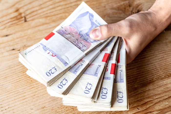 hand holding bundles of twenty pound notes
