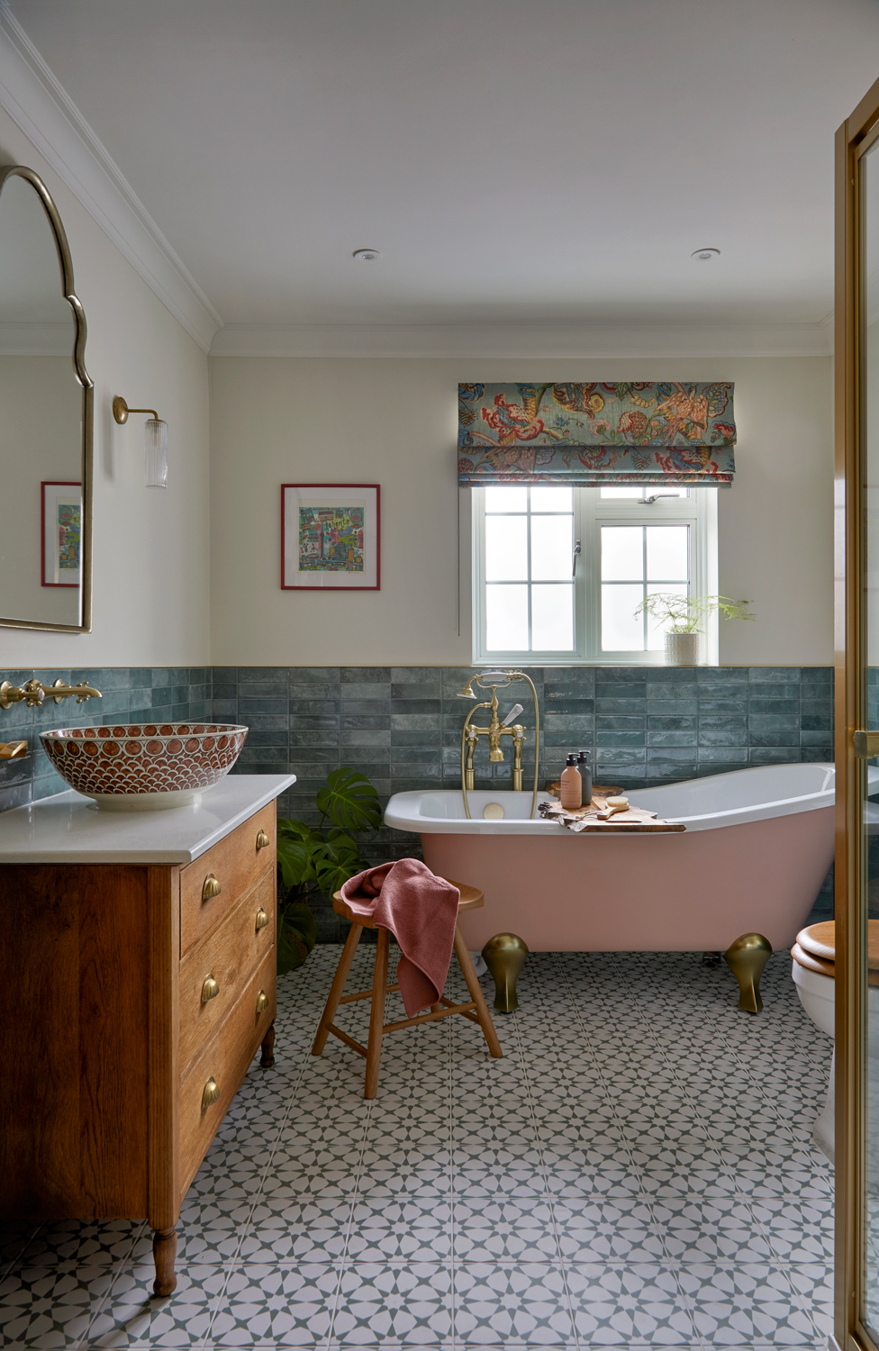 A stylish bathroom with a soft pink freestanding bath, brass fittings, and patterned floor tiles. Green glazed wall tiles and a colourful Roman blind add character, while a wooden vanity with a patterned basin brings warmth to the space. A stylish bathroom with a soft pink freestanding bath, brass fittings, and patterned floor tiles. Green glazed wall tiles and a colourful Roman blind add character, while a wooden vanity with a patterned basin brings warmth to the space.