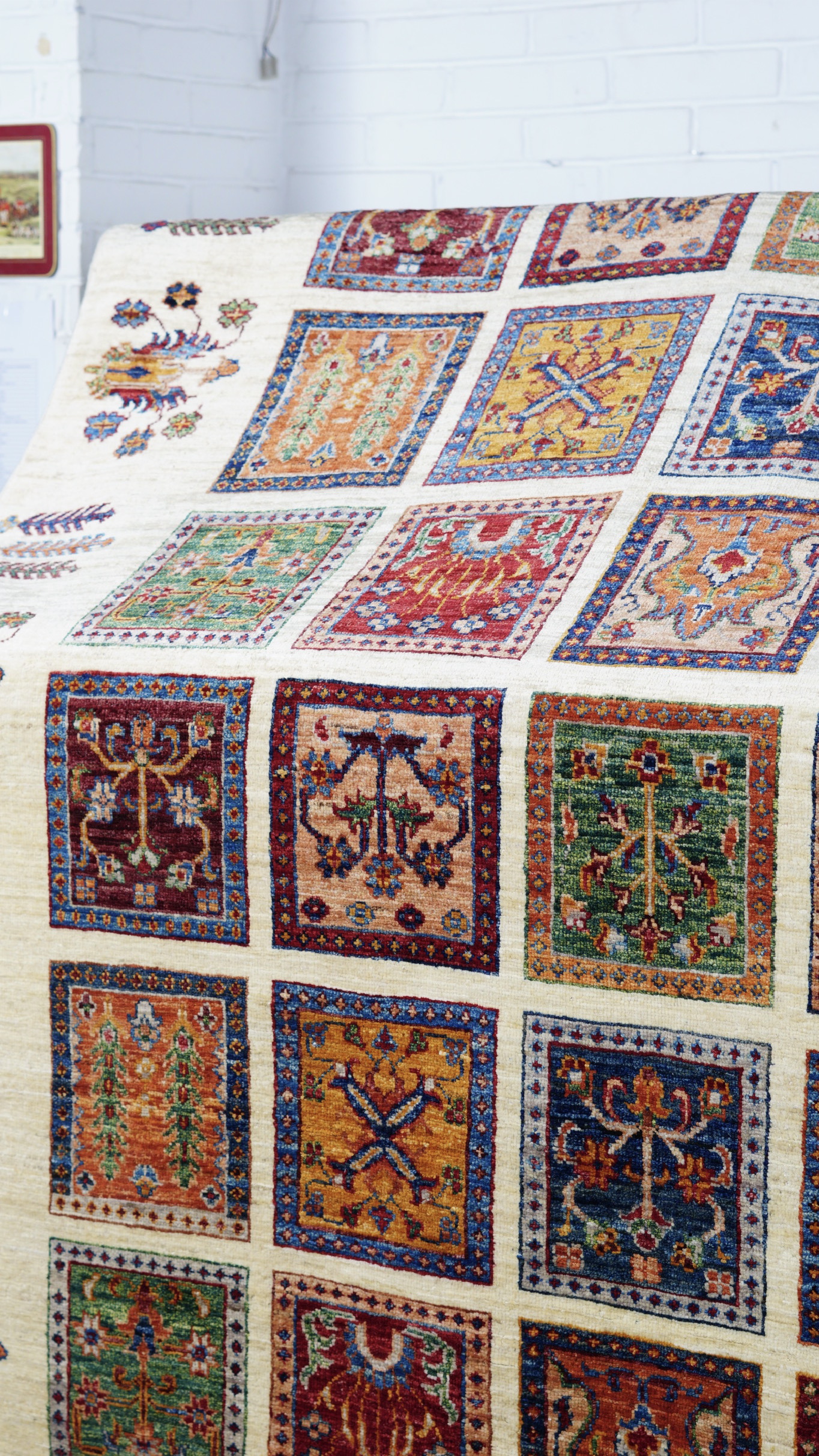 A close-up, angled view of a hand-knotted Afghan Super Kazak rug, featuring a "garden" design with a grid of colourful, individual geometric squares on a cream background.