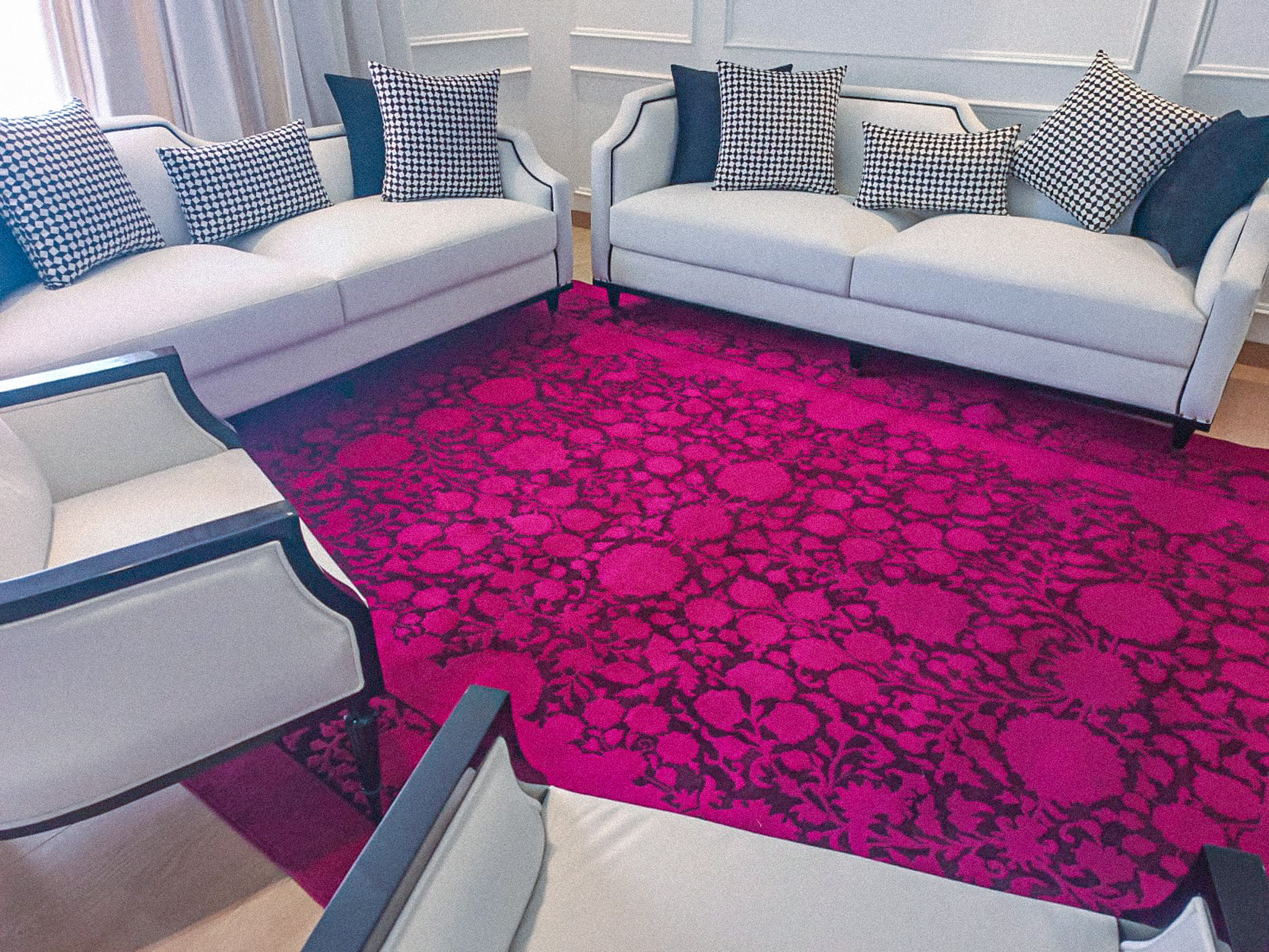 A bright, fuchsia-pink rug with a dark, oversized floral pattern, placed in a formal living room between white sofas and chairs with houndstooth cushions.