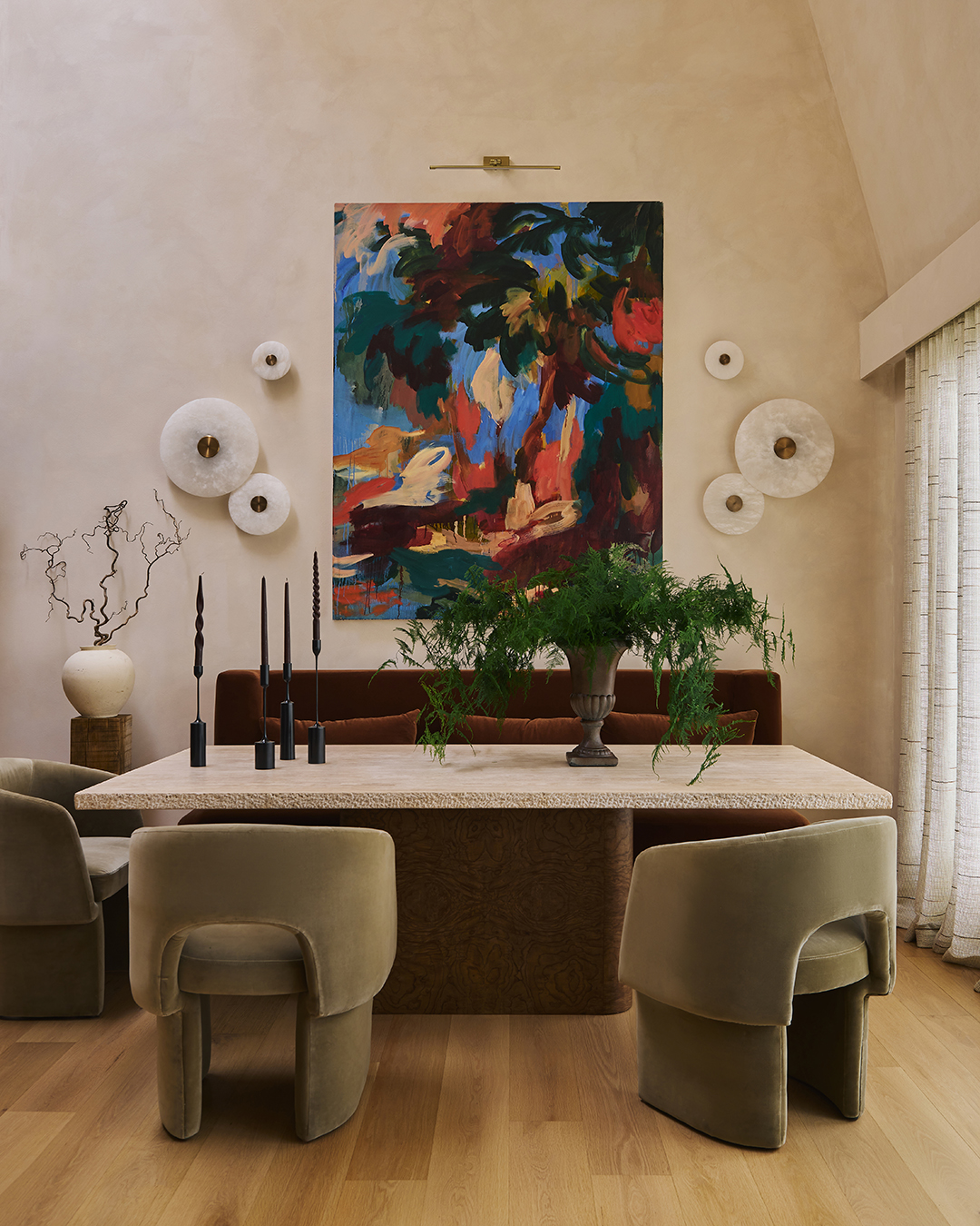 A refined dining setting where sculptural furniture, soft architectural lines, and a restrained material palette are anchored by a bold artwork, creating a composed yet expressive focal point.