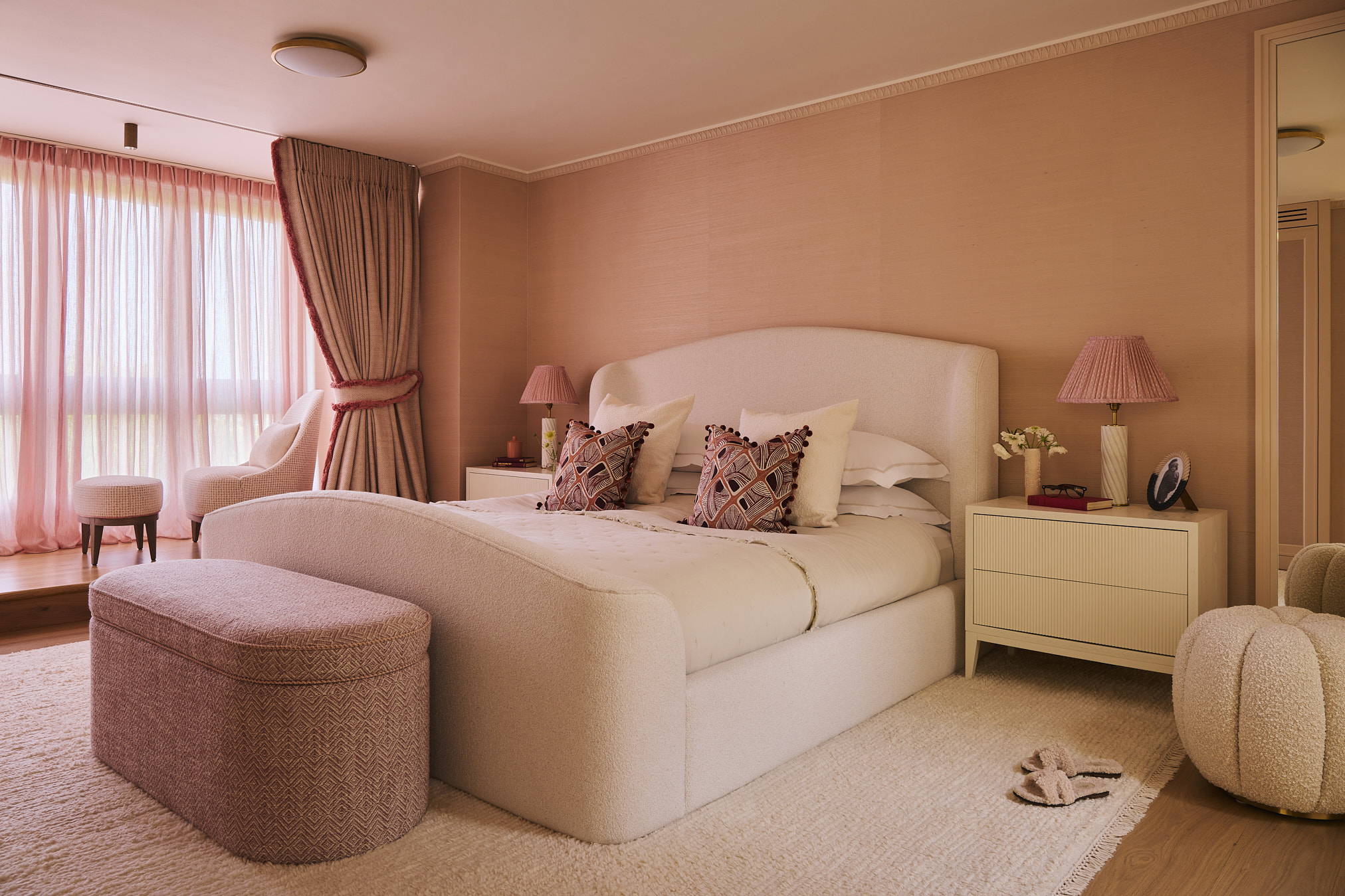 A soft, layered master bedroom defined by warm tones, upholstered forms, and diffused light, creating a calm and enveloping atmosphere for rest.