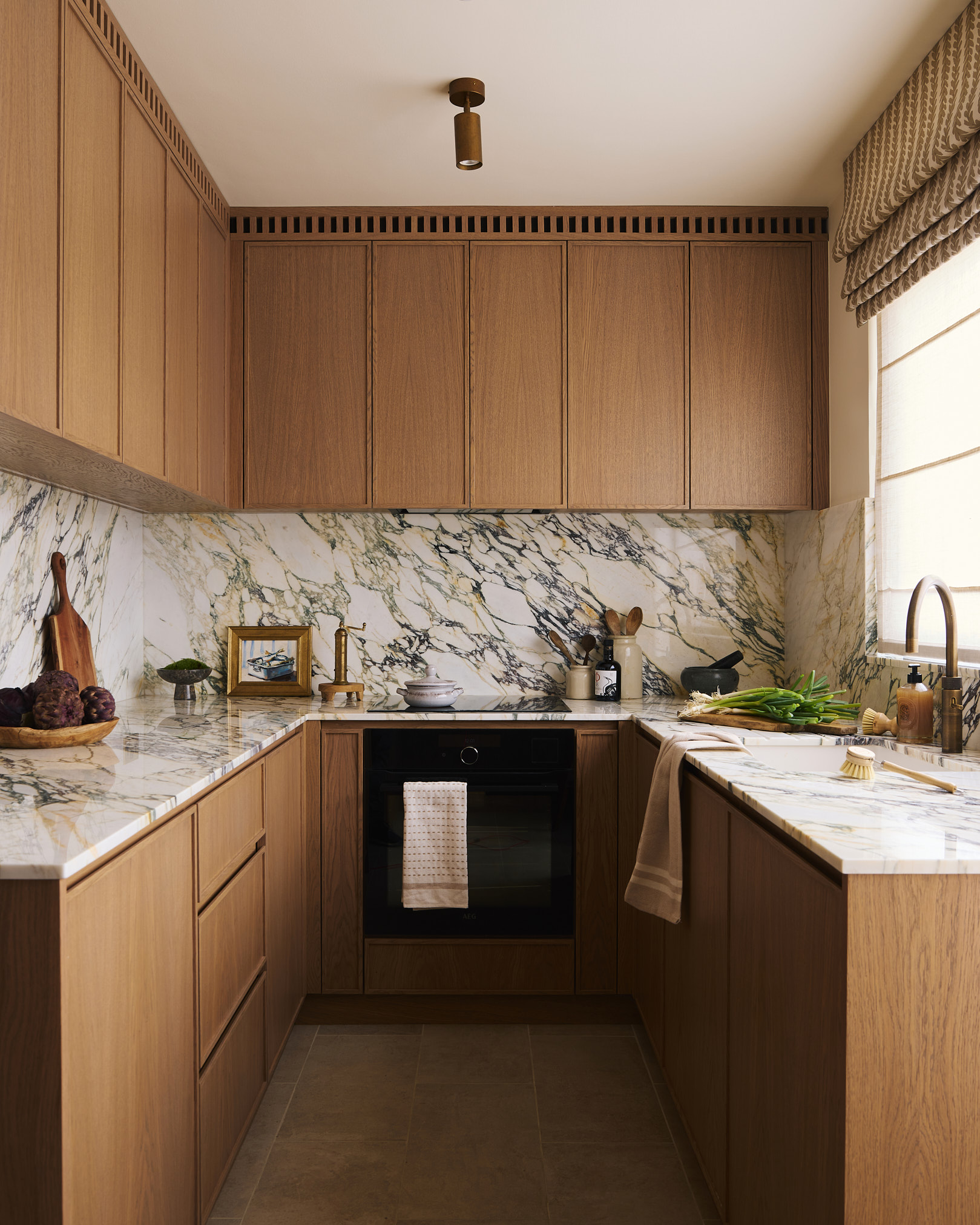 A compact kitchen defined by clean lines and warm oak cabinetry, paired with a richly veined marble backsplash that introduces depth and contrast within a restrained, functional layout.