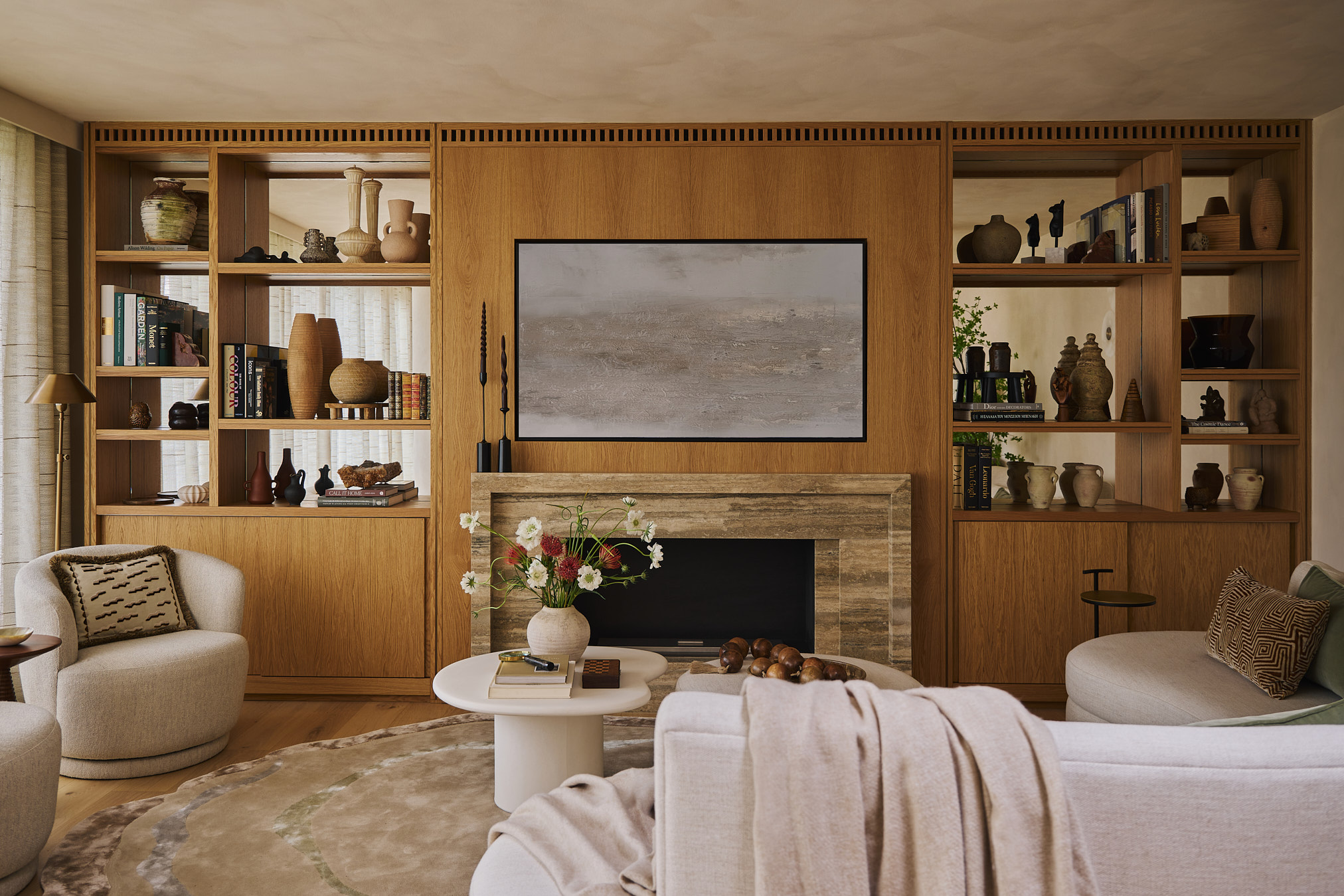 A calm, materially rich living space defined by bespoke oak joinery, integrated storage, and a sculptural curved seating arrangement, creating a balanced composition that centres on warmth, texture, and quiet functionality.