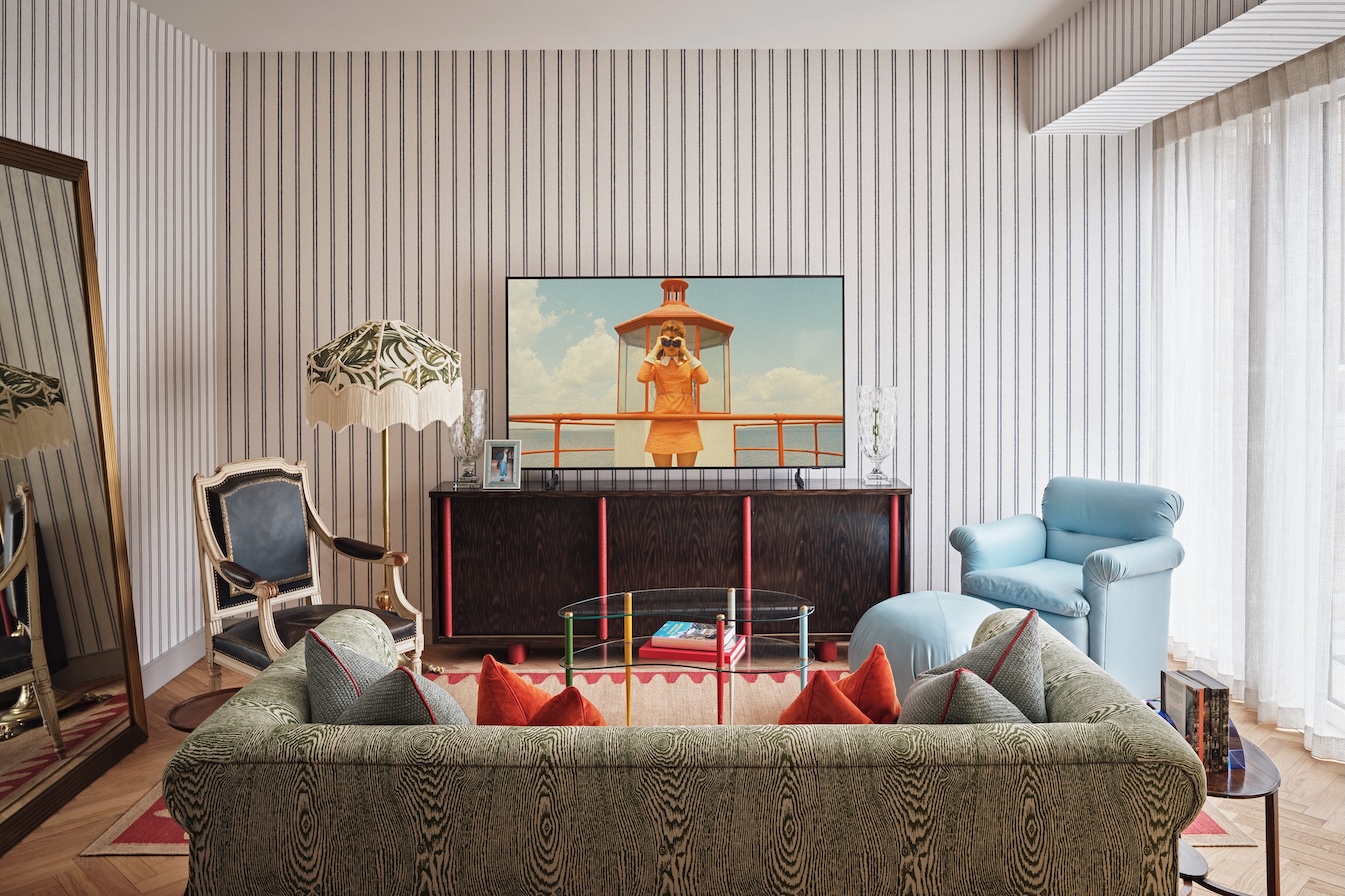 Living room with bold striped Phillip Jeffries wallpaper, bespoke green sofa, and primary color accents