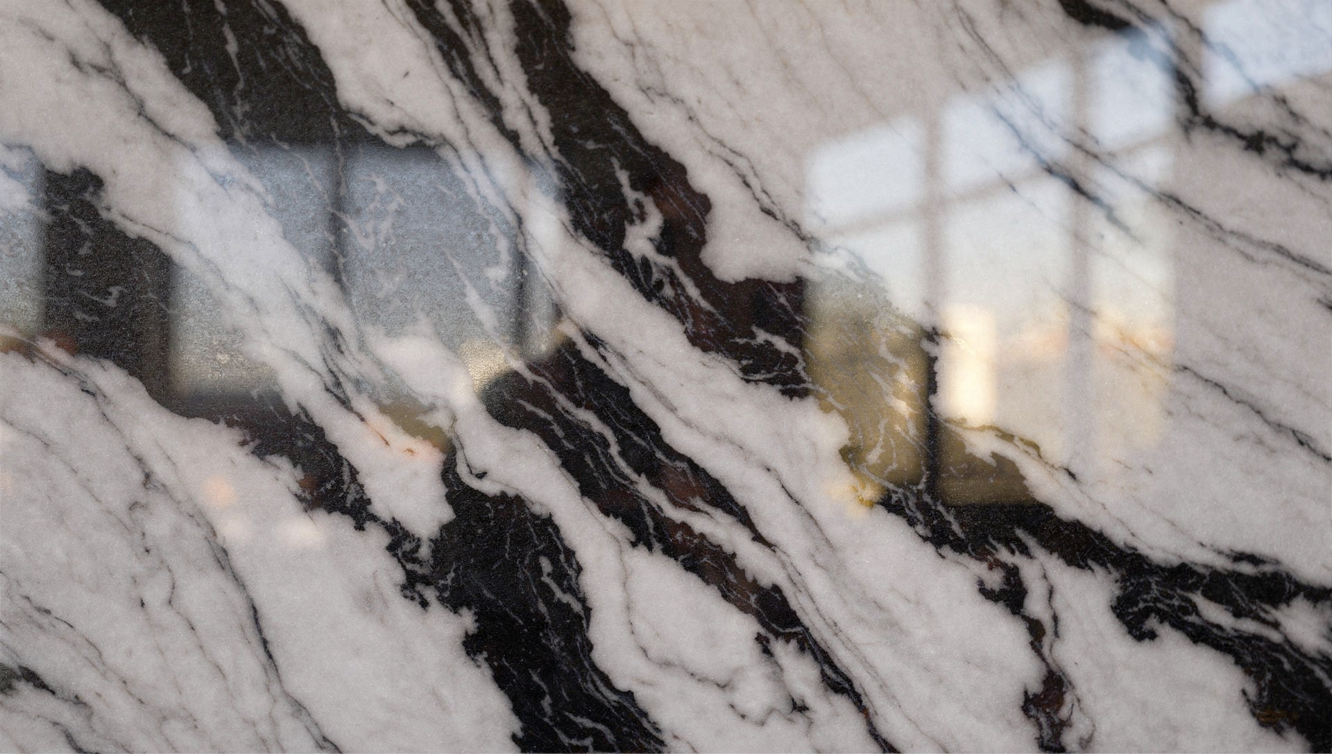 Extreme close-up of polished Panda White marble with bold black veining and soft window reflections across the surface.