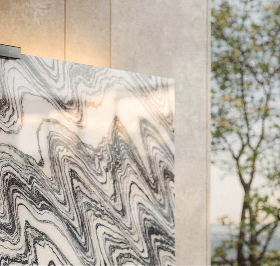 Close-up of Fantastico marble with flowing black-and-white veining and warm halo backlight glowing behind the slab edge.