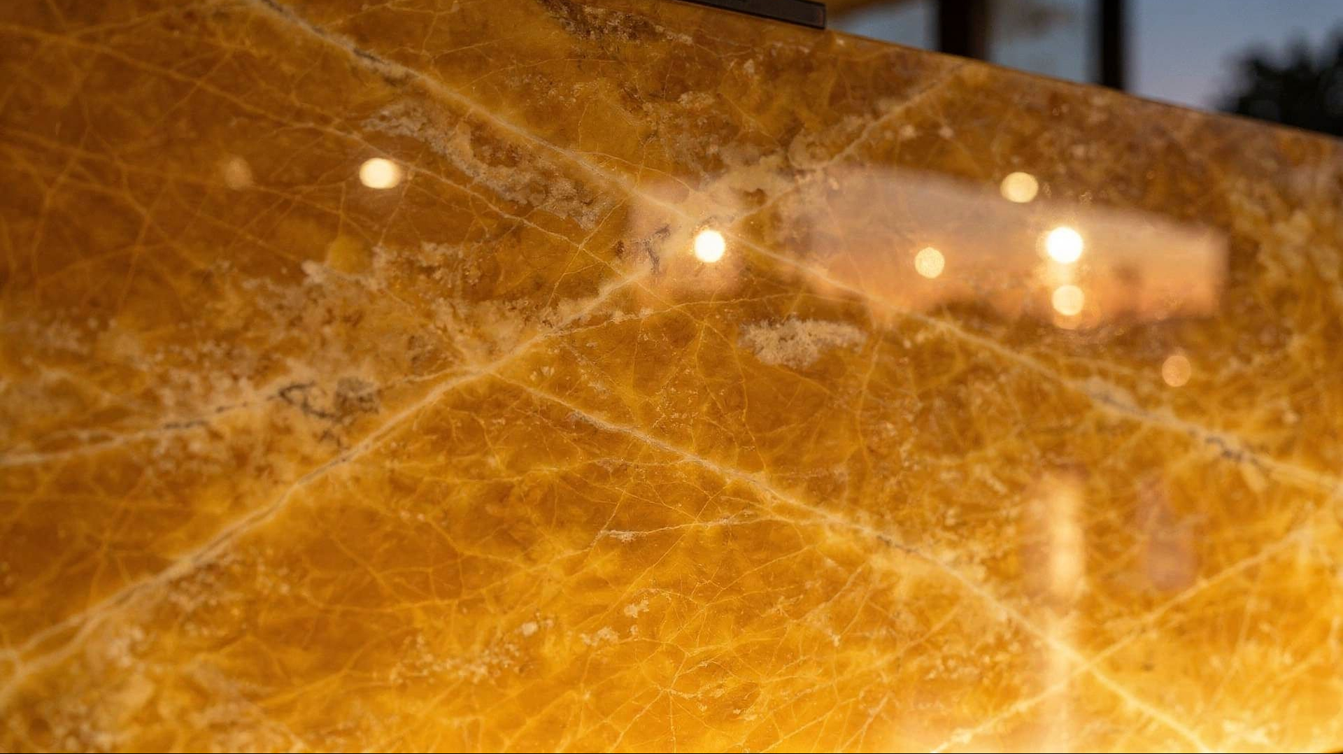 Close-up of illuminated polished yellow onyx with warm amber translucency, soft reflections, and the black top clamp of the art object visible above the stone.