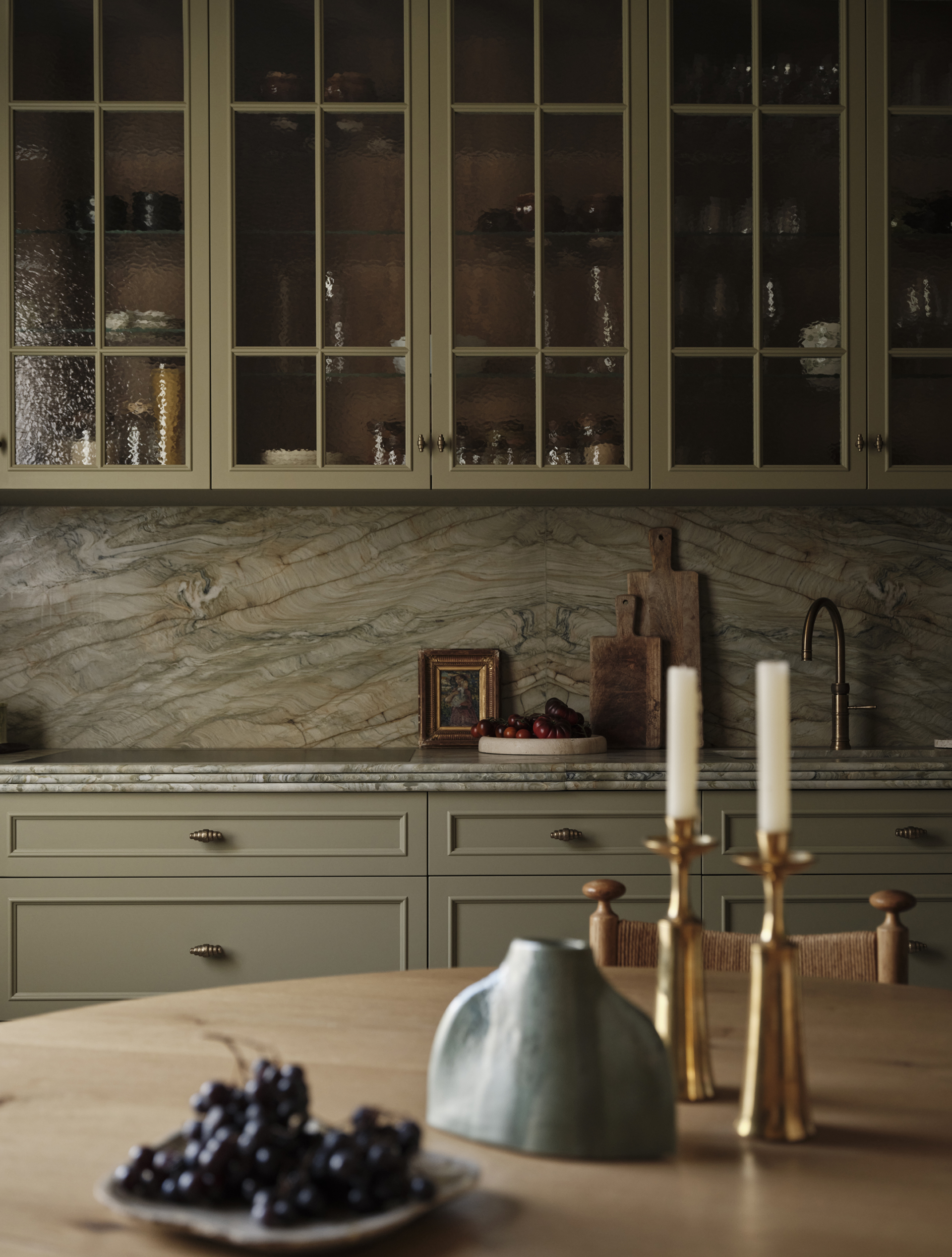 Sage-green kitchen cabinetry with glazed upper cupboards, a veined stone splashback and a timber island in the foreground.