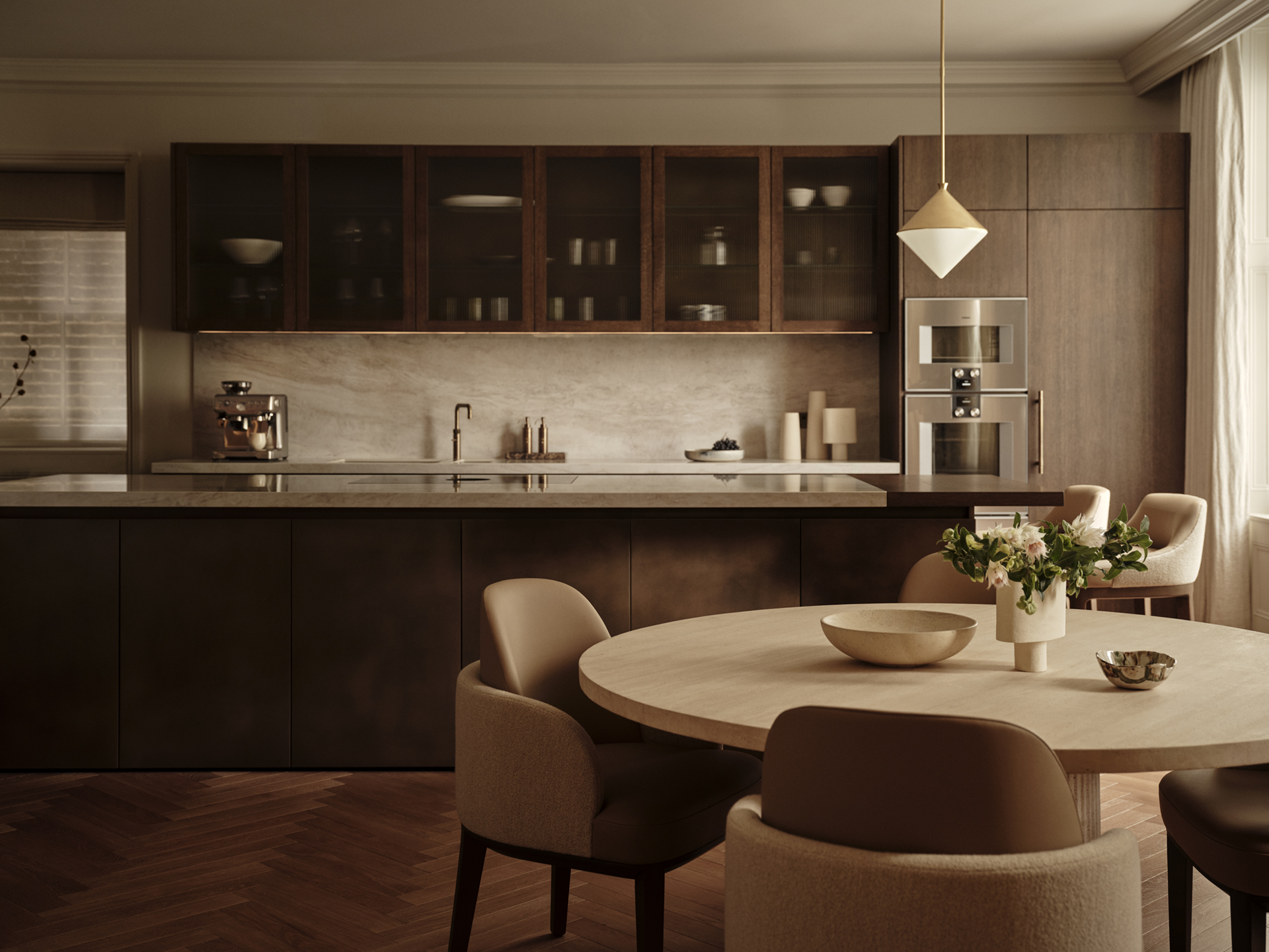 Dark timber kitchen cabinetry with glazed upper cupboards and a pale stone splashback, overlooking a round dining table with upholstered chairs.