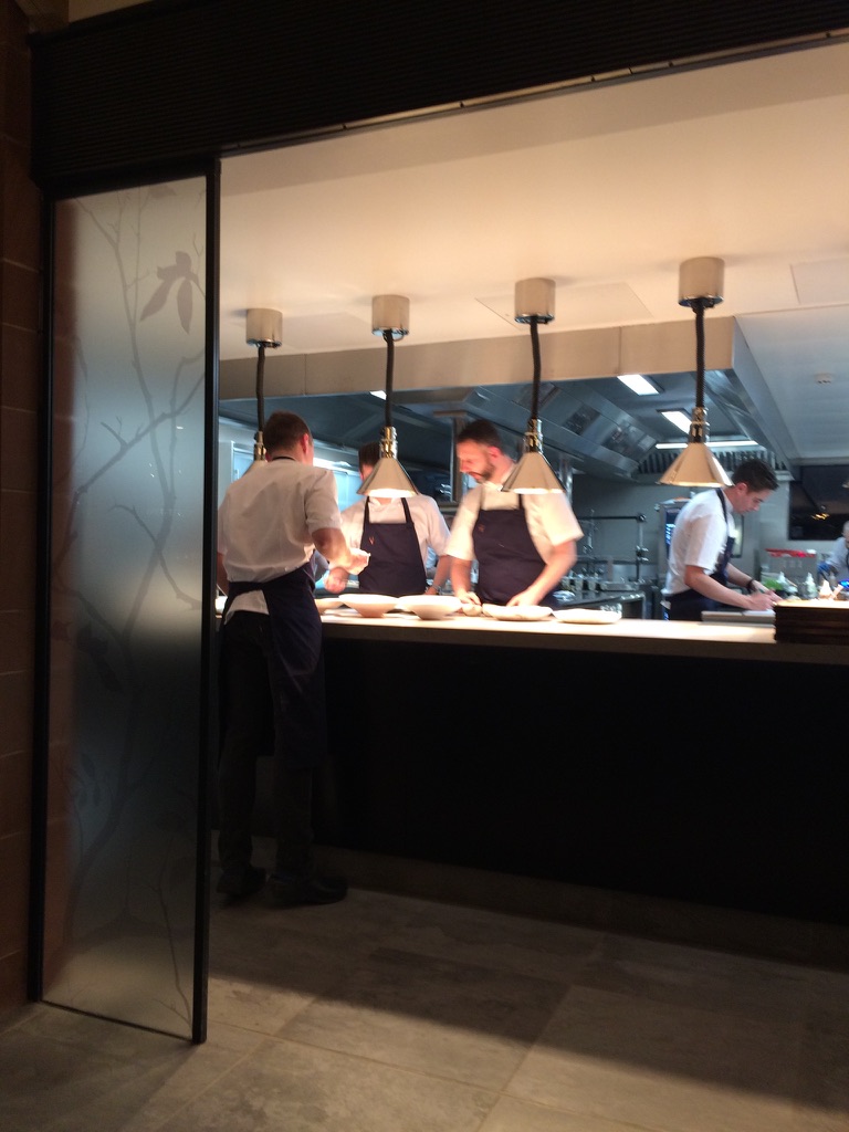 Open kitchen at Moor Hall restaurant, Aughton, showing chefs preparing dishes at the pass beneath pendant lighting.