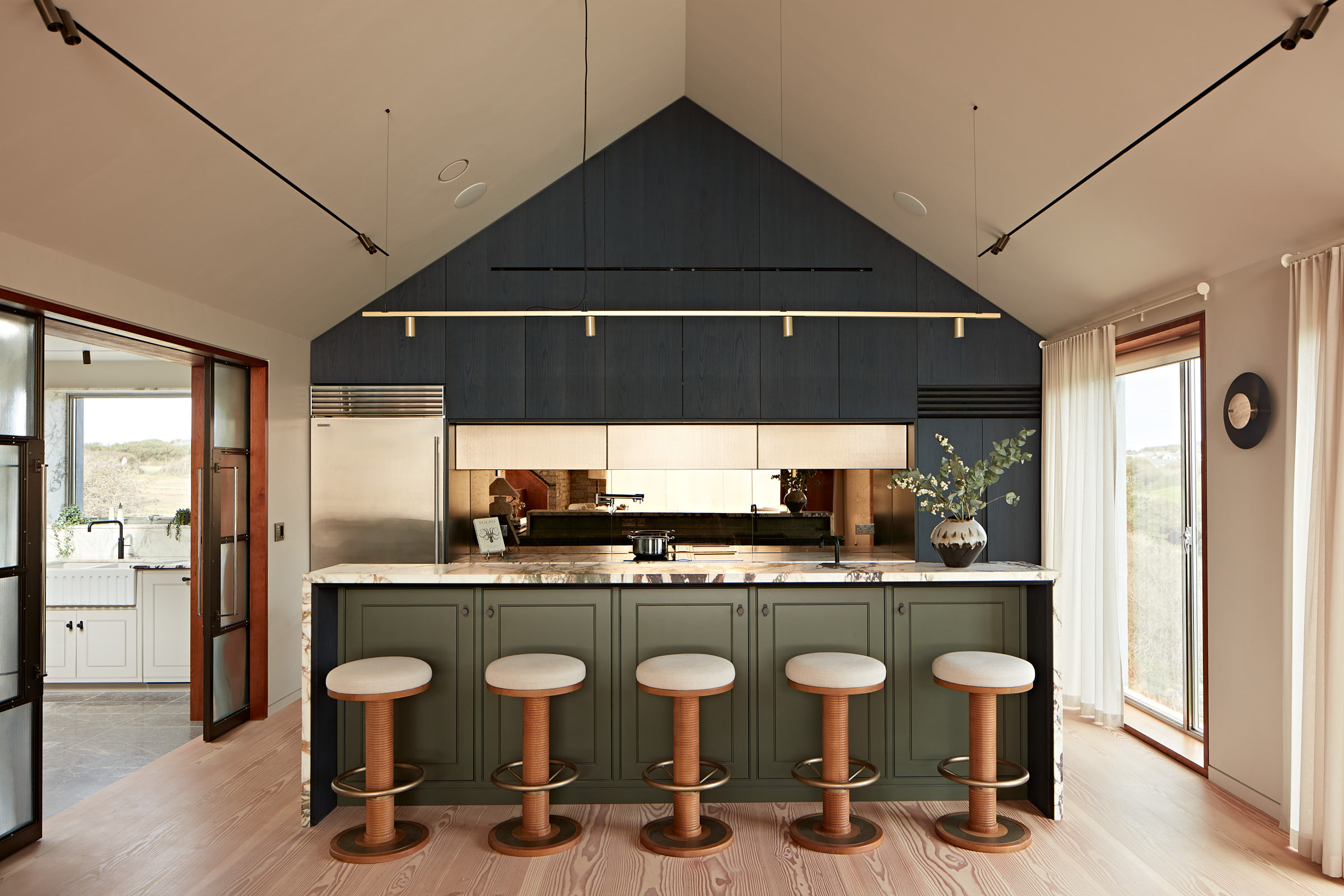 Dark toned kitchen with bronze mirrored splash back, pitched ceiling, marble island and 5 bar stools
