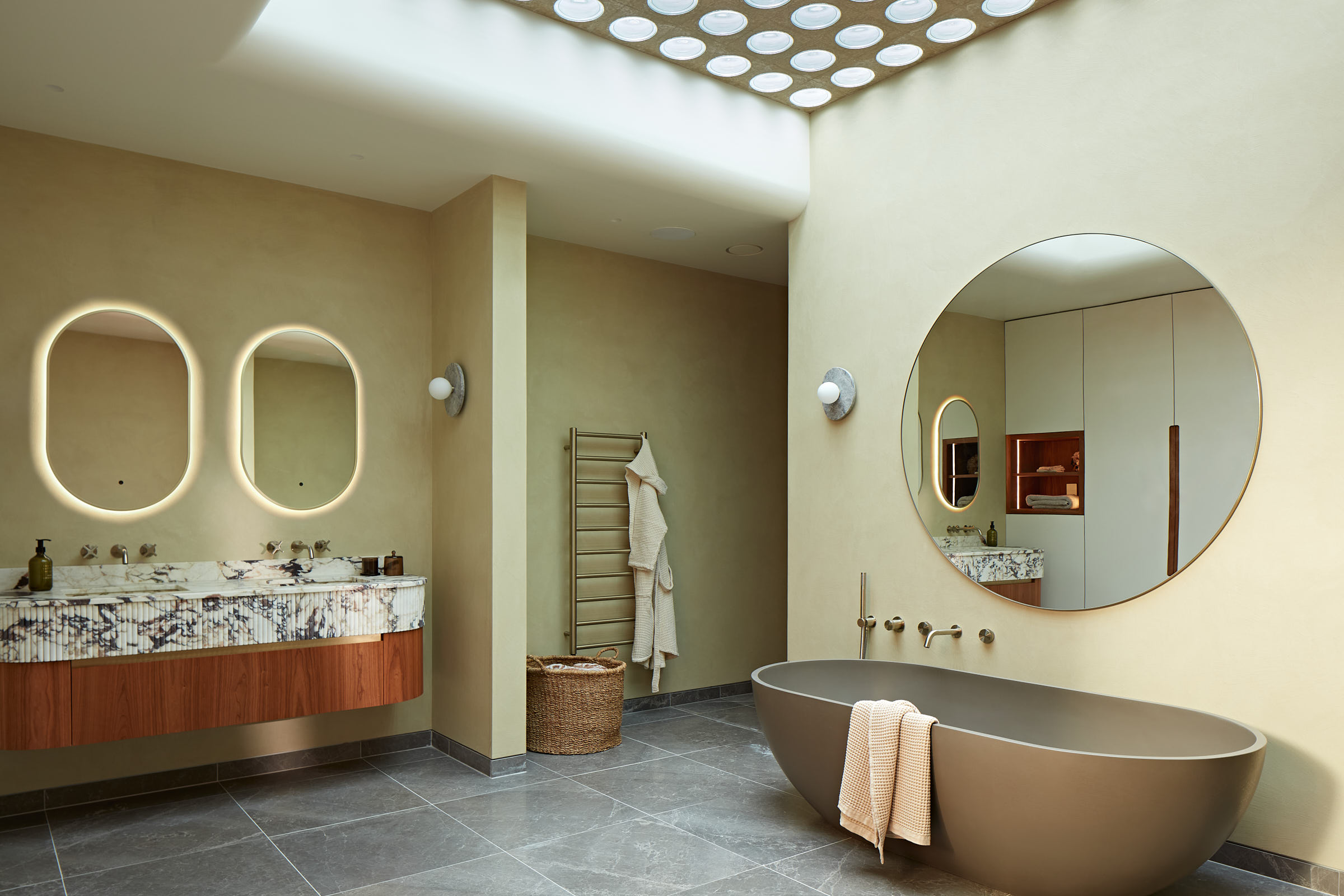 Spacious bathroom with freestanding bath,  large round mirror and double marble vanity unit