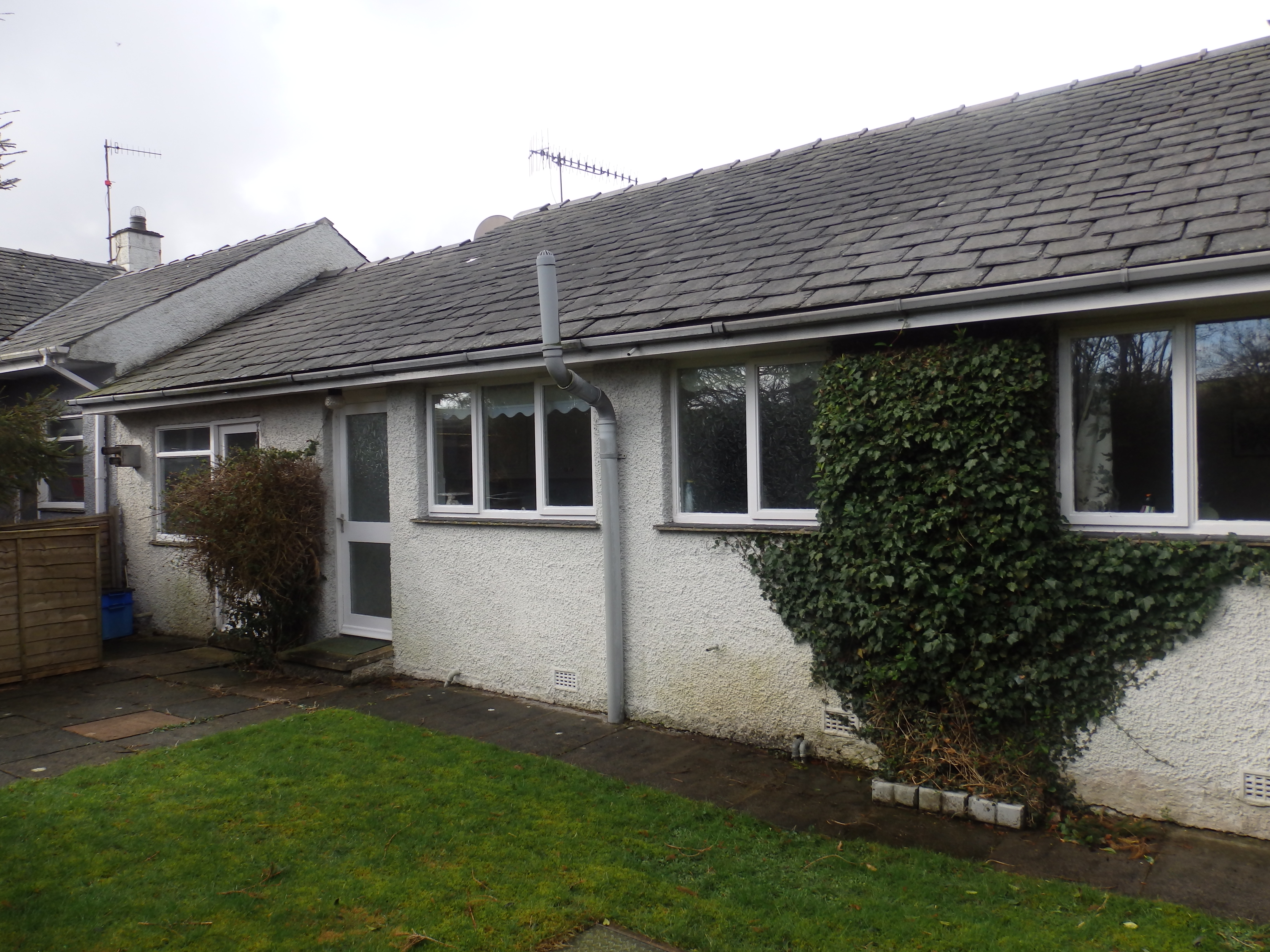 Original single-storey bungalow before its extensive redesign and reconstruction, showing the dated exterior, traditional windows and overgrown ivy.