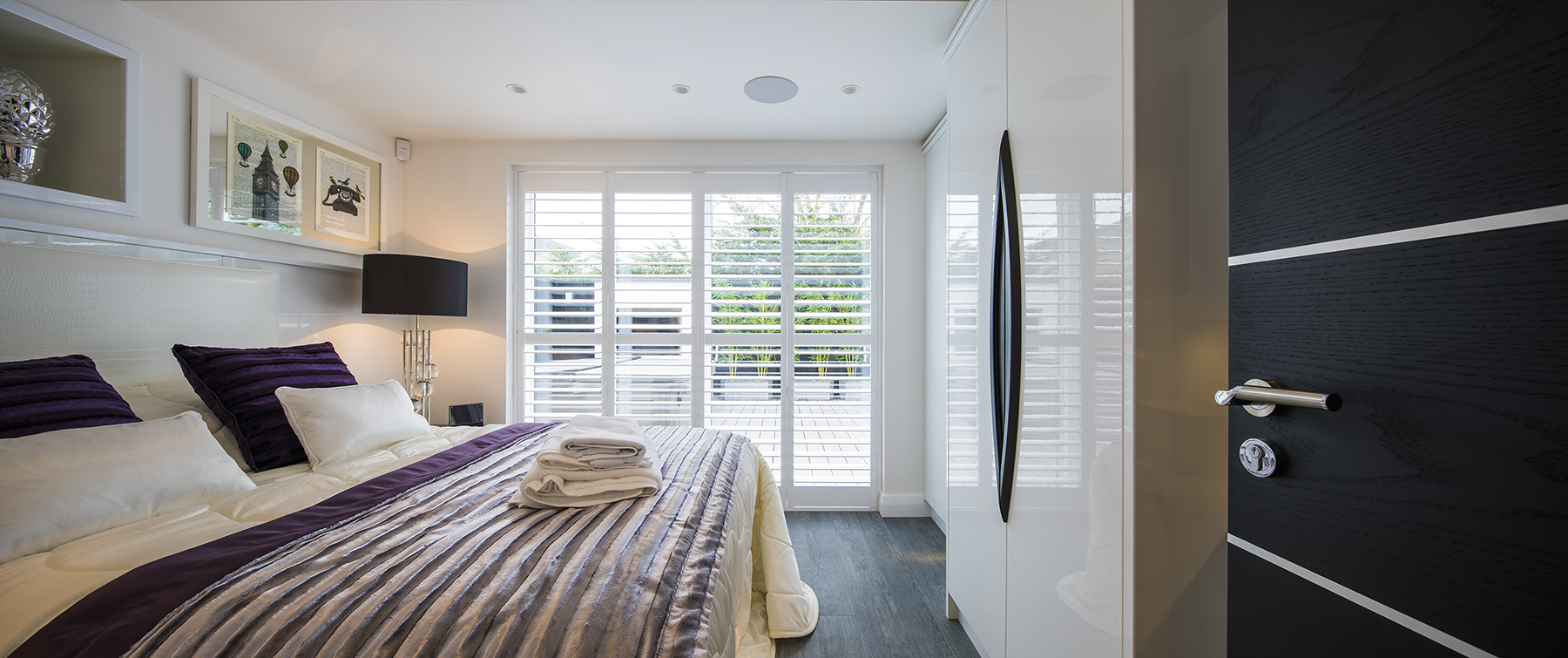Contemporary bedroom featuring bespoke fitted furniture, luxurious layered bedding and large windows overlooking the landscaped gardens.