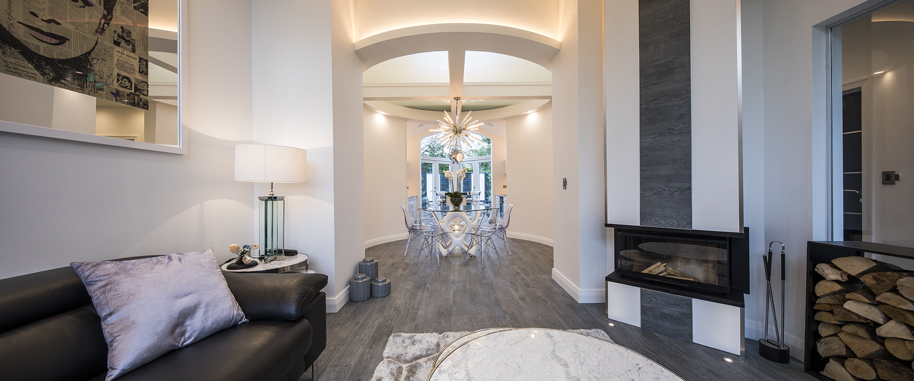 Contemporary open-plan living room featuring a bespoke fireplace, dark timber flooring, modern furnishings and views through to the dining area.