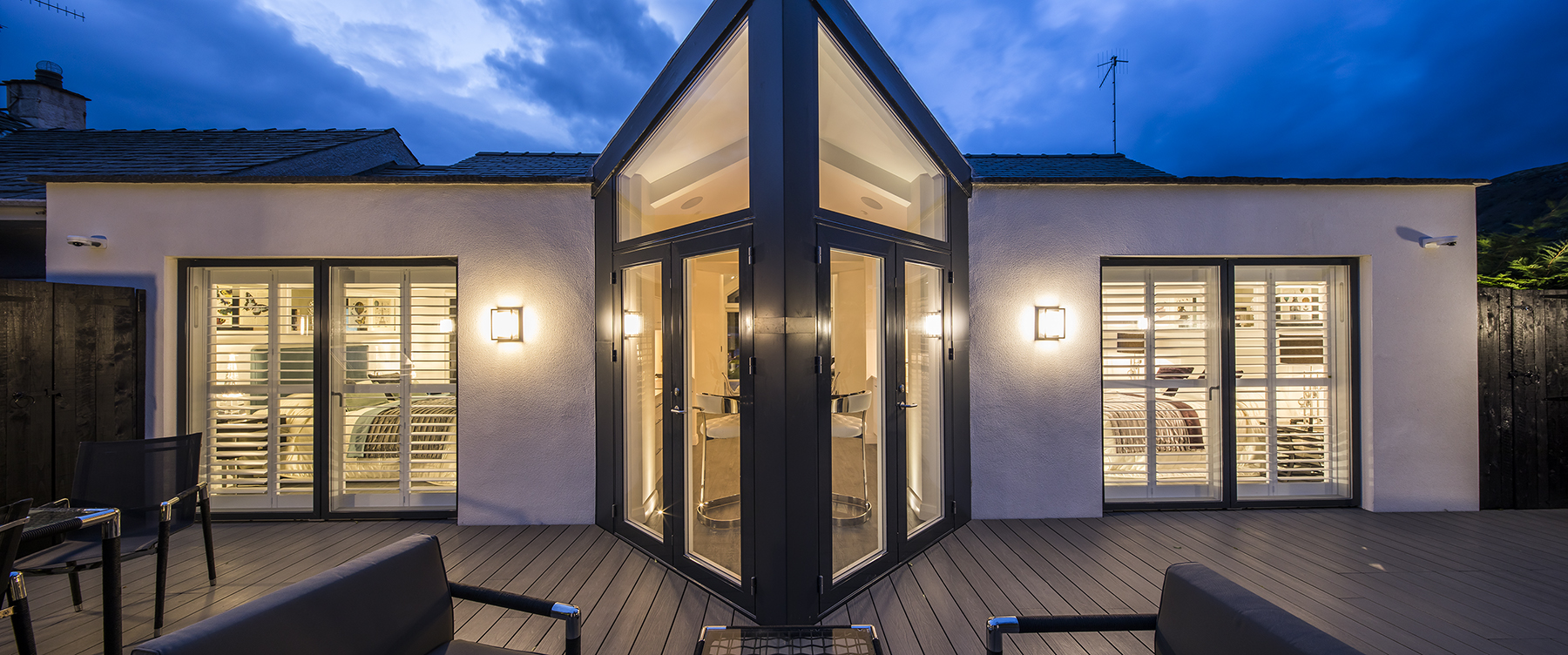 Contemporary rear elevation featuring a striking angular glazed entrance, full-height bedroom glazing and landscaped outdoor entertaining terrace.