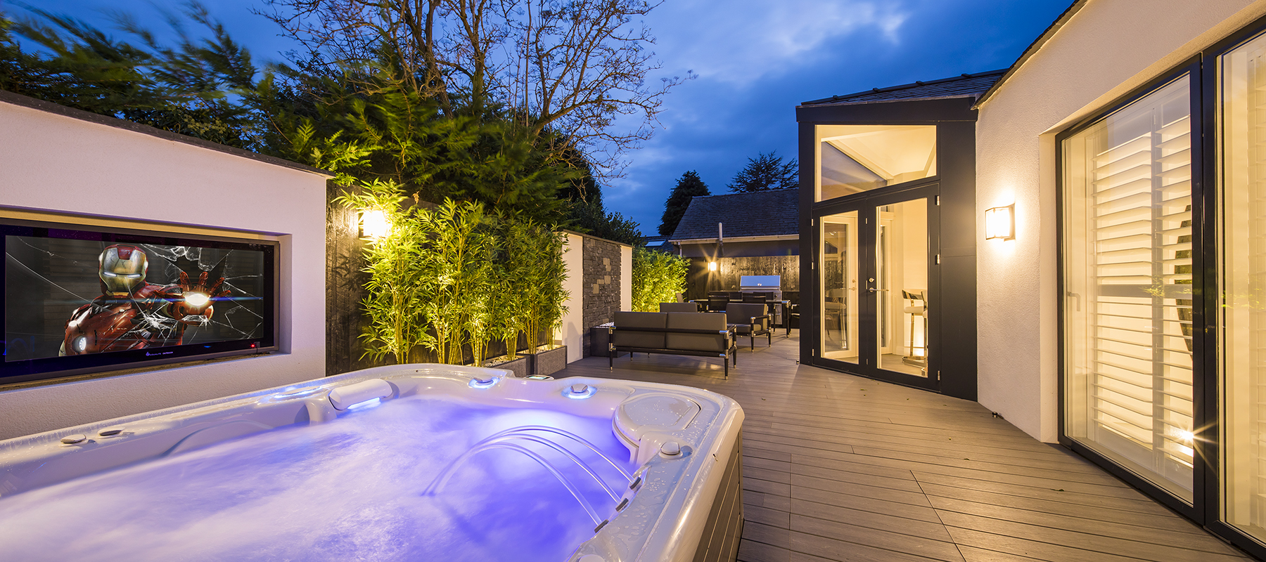 Landscaped private terrace at dusk featuring an illuminated swim spa, contemporary glazing, outdoor seating and architectural garden lighting.