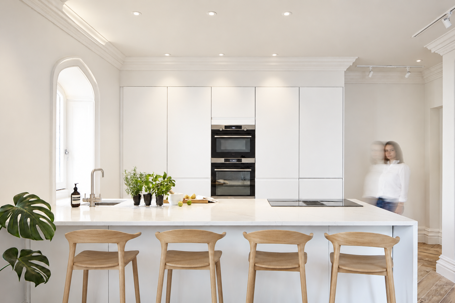 Contemporary white kitchen with a quartz island and oak bar stools in Grade II-listed Carter Manor, Wilmslow.