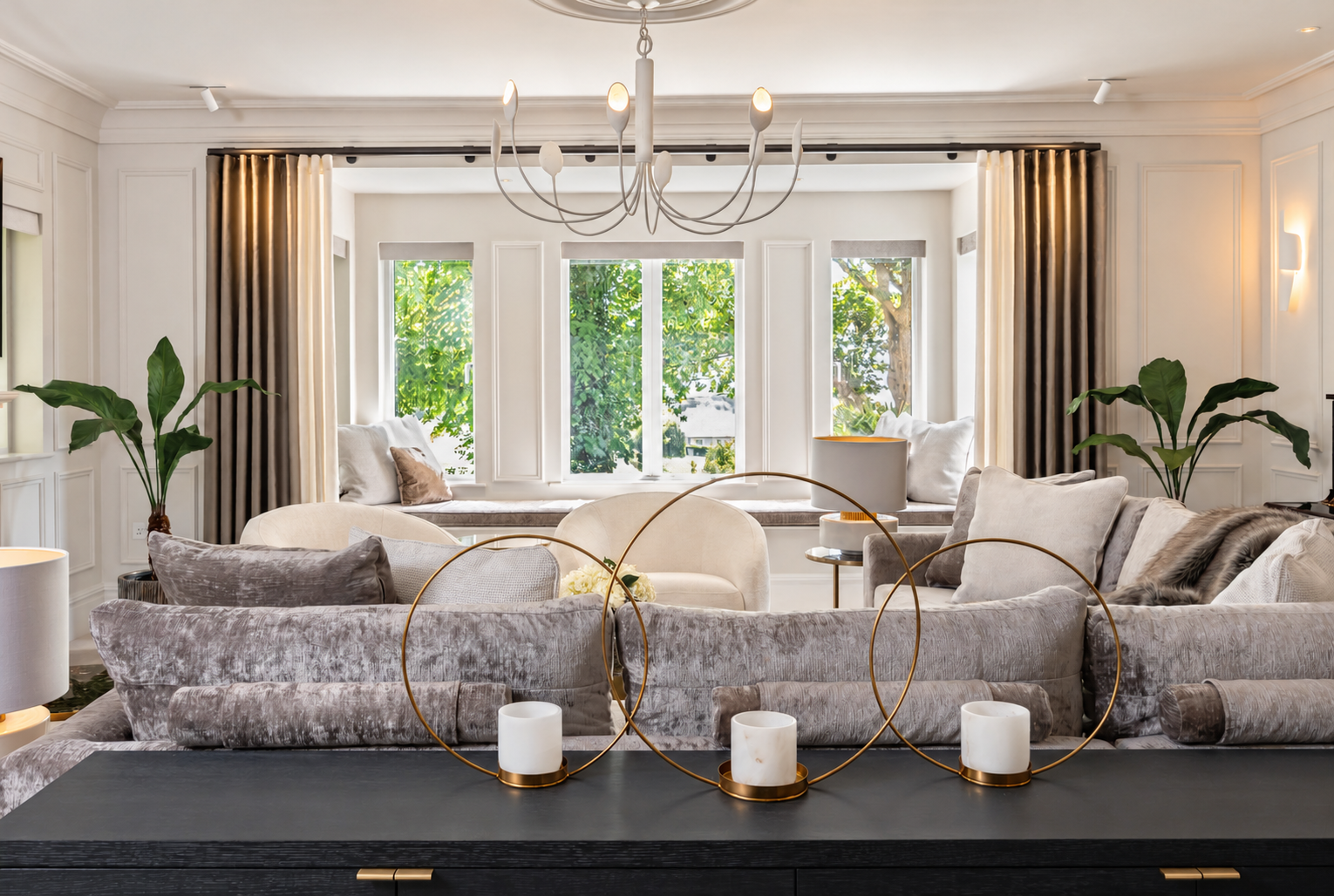 Grey velvet sofa, curved cream chairs and a bay window seat beneath a white sculptural chandelier at Hillcrest House.