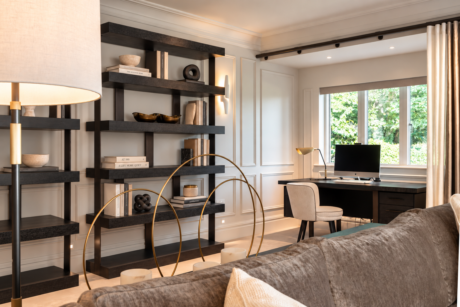 Desk beneath a window with dark shelving, a monitor and upholstered chair in the panelled Hillcrest House living room.