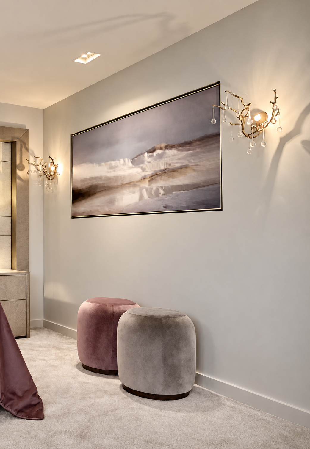 Bedroom landscape artwork flanked by decorative wall lights above velvet footstools.