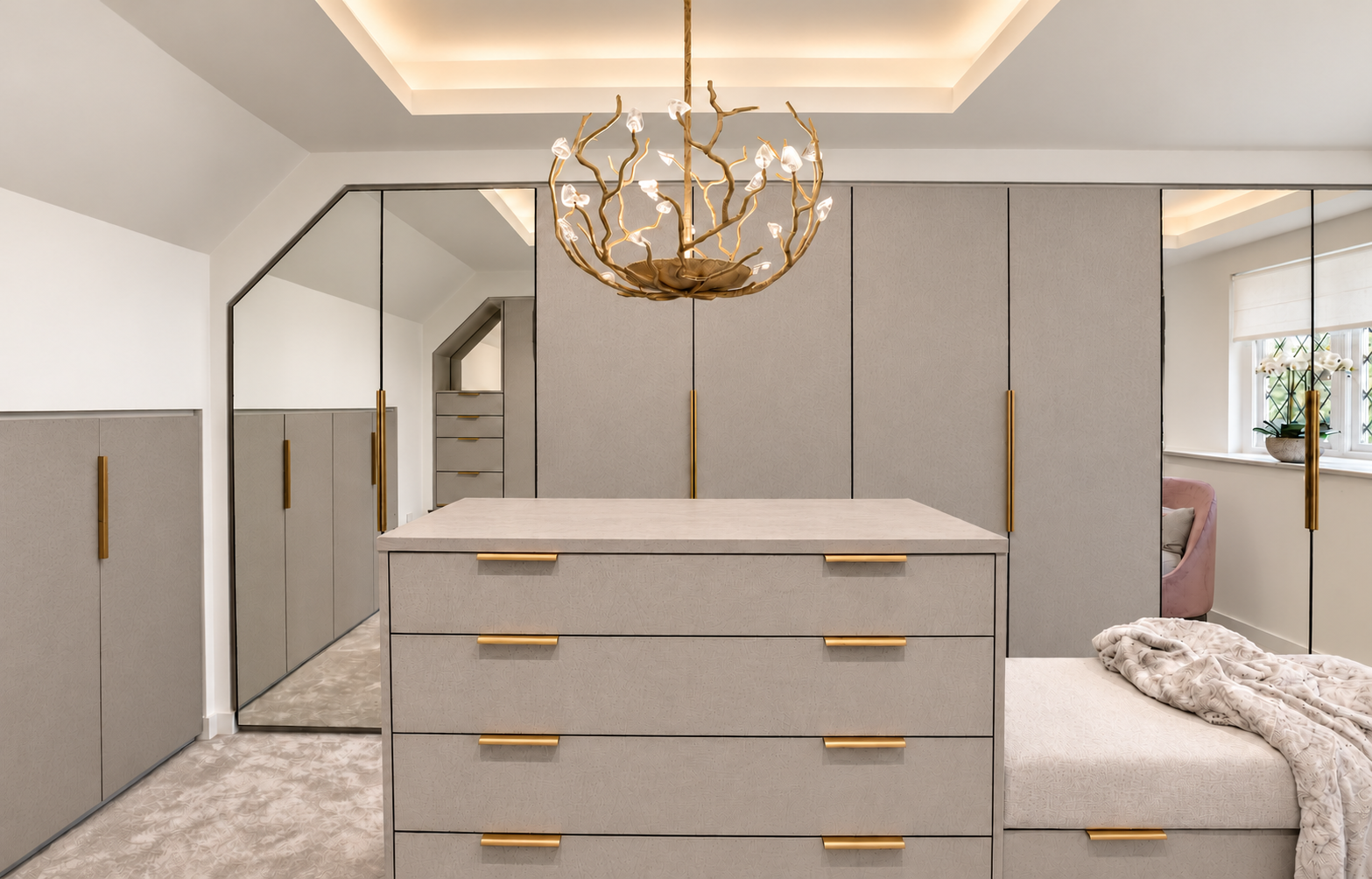 Dressing room island with brass pulls beneath a Porta Romana Blossom chandelier.