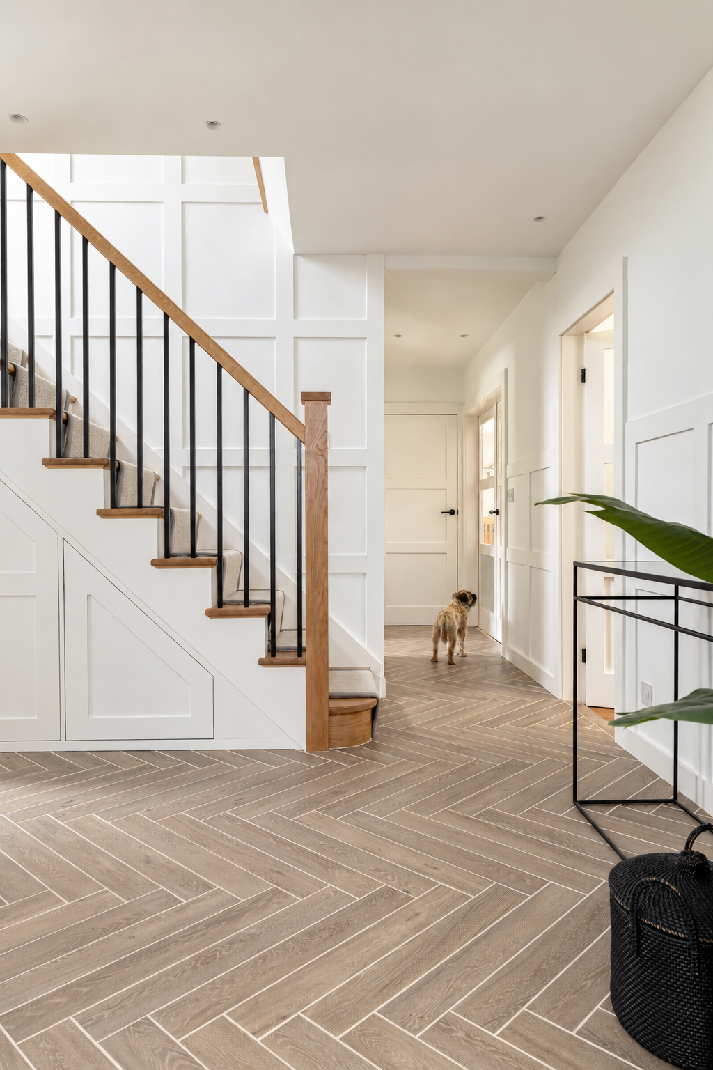 Panelled hallway with herringbone flooring, an oak staircase and a slim console table with greenery.
