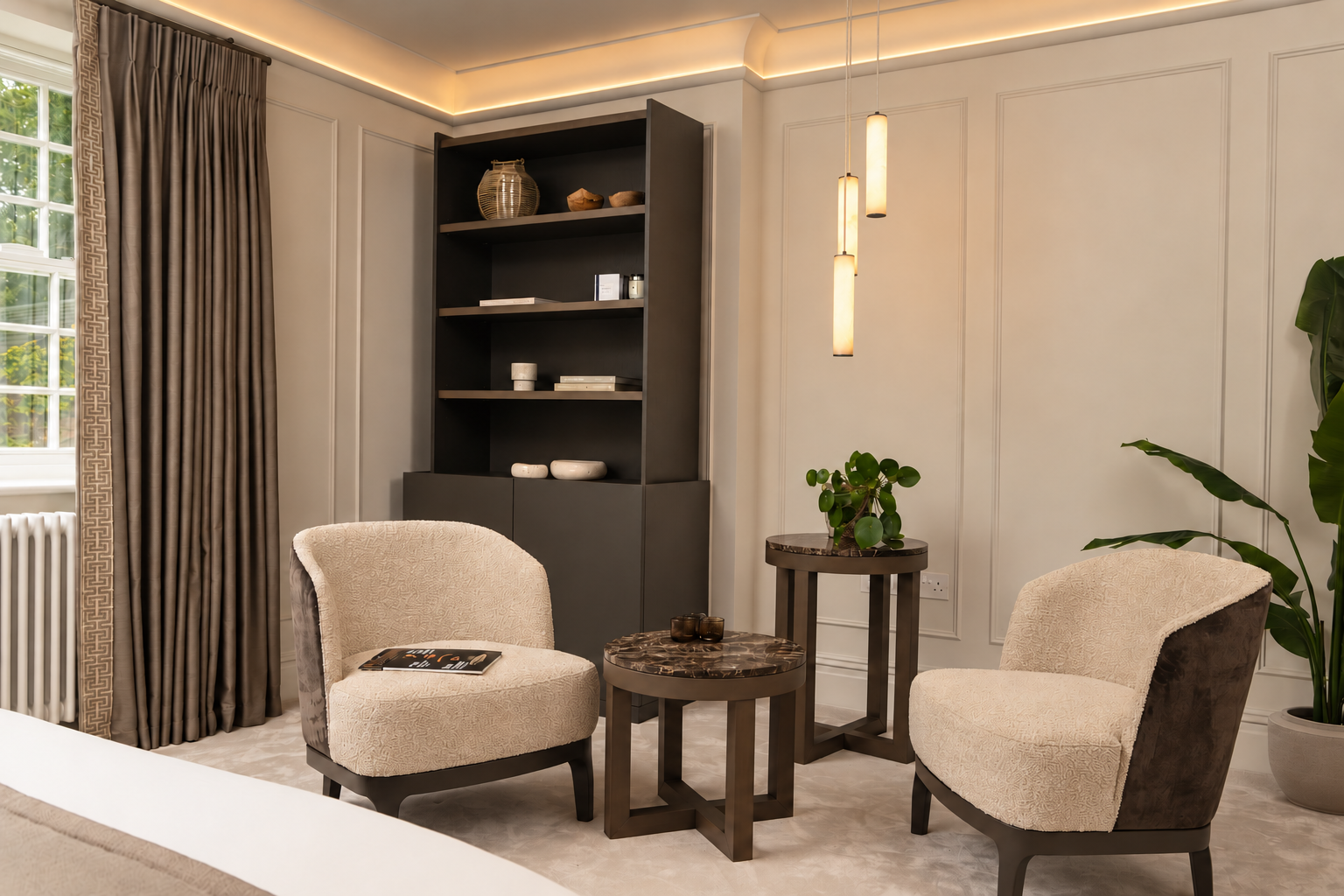 Bedroom seating area with cream chairs, round tables and three glowing cylindrical pendants.
