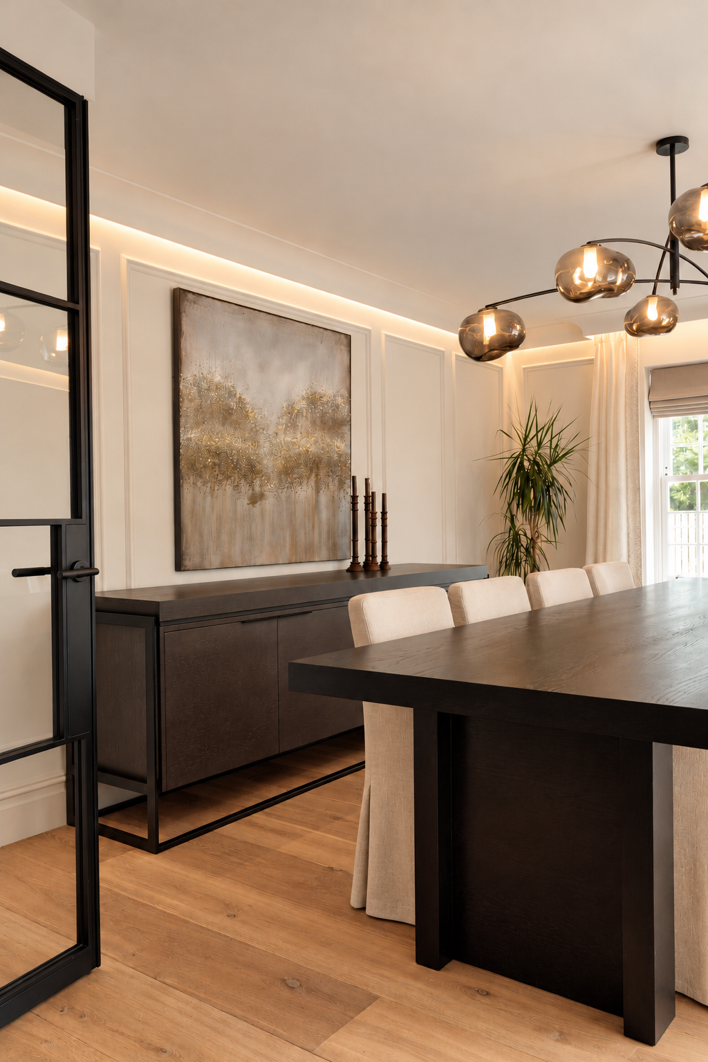 Dining table and upholstered chairs beside a dark sideboard, abstract artwork and smoked-glass pendant light.
