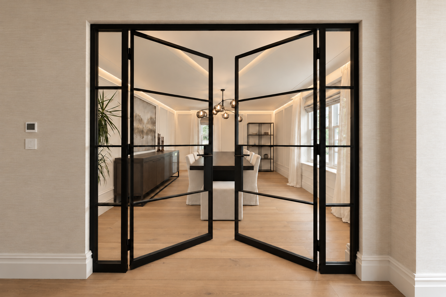 View through open black-framed glazed doors into the dining room, with a dark table and cream chairs.