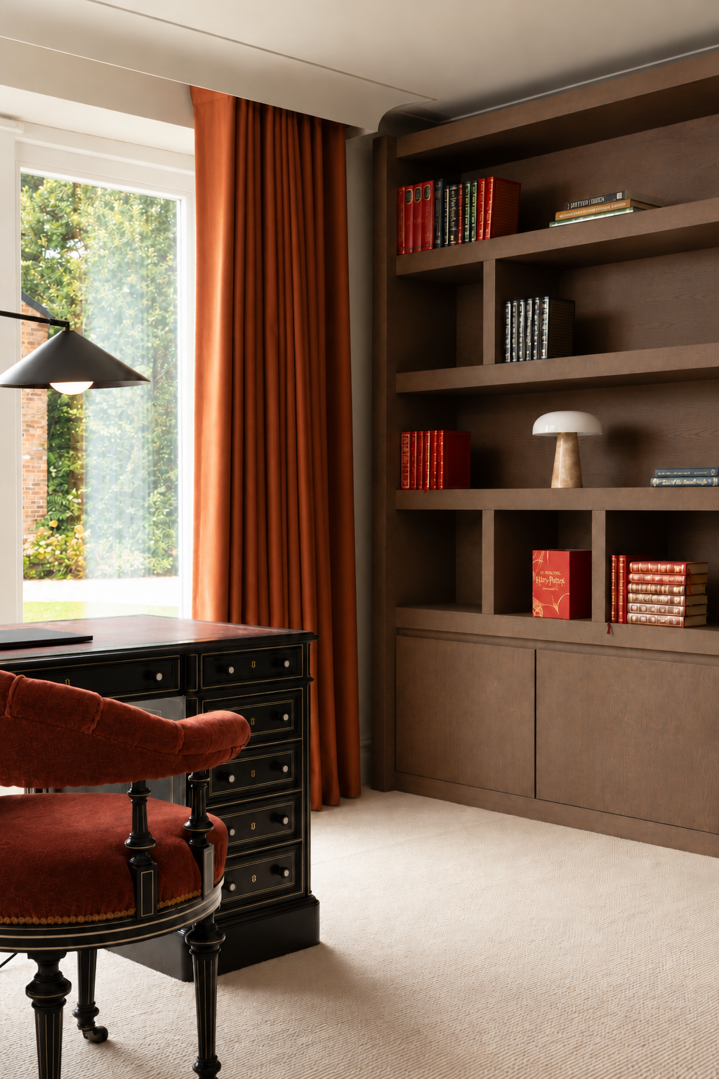 Antique desk and rust upholstered chair beside timber cabinetry and full-length rust curtains.