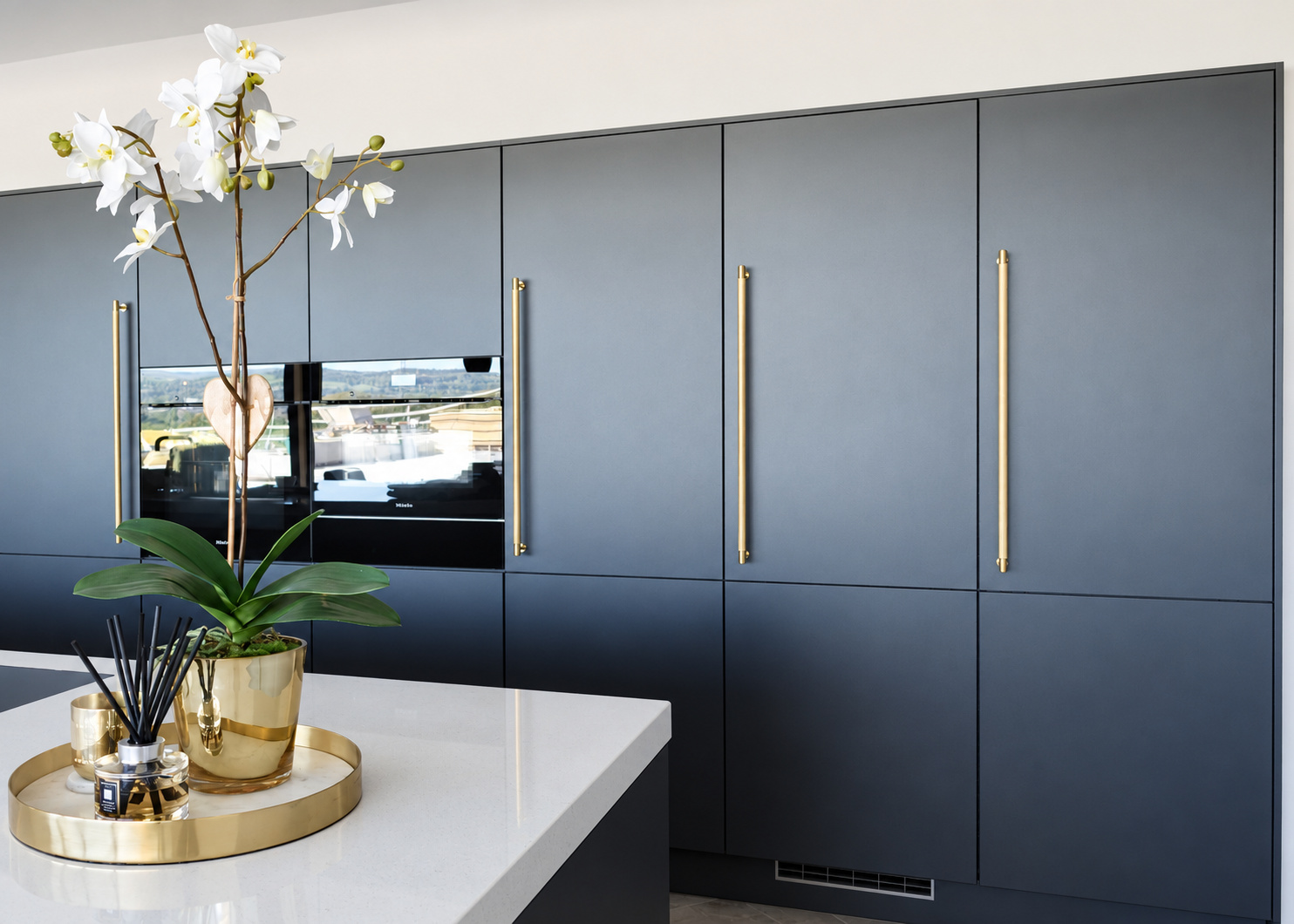 Dark kitchen cabinetry with long brass handles and integrated ovens at The Upton, Prestbury.