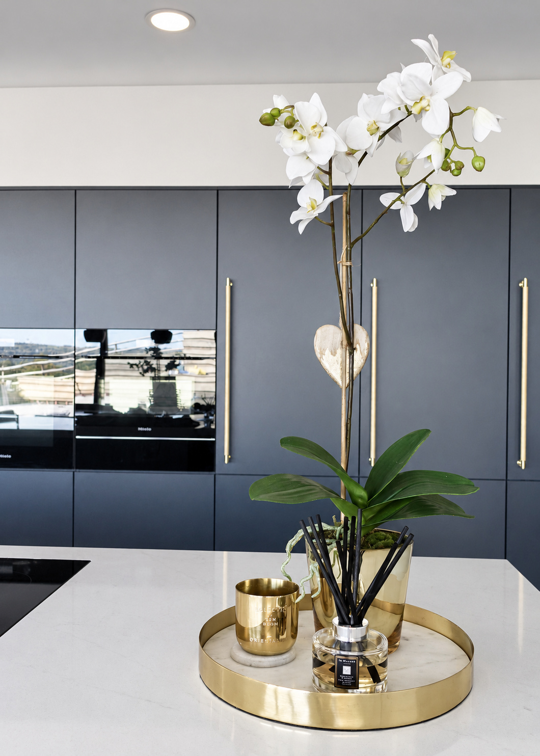 White orchid and brass accessories on a kitchen island beside dark cabinetry at The Upton, Prestbury.
