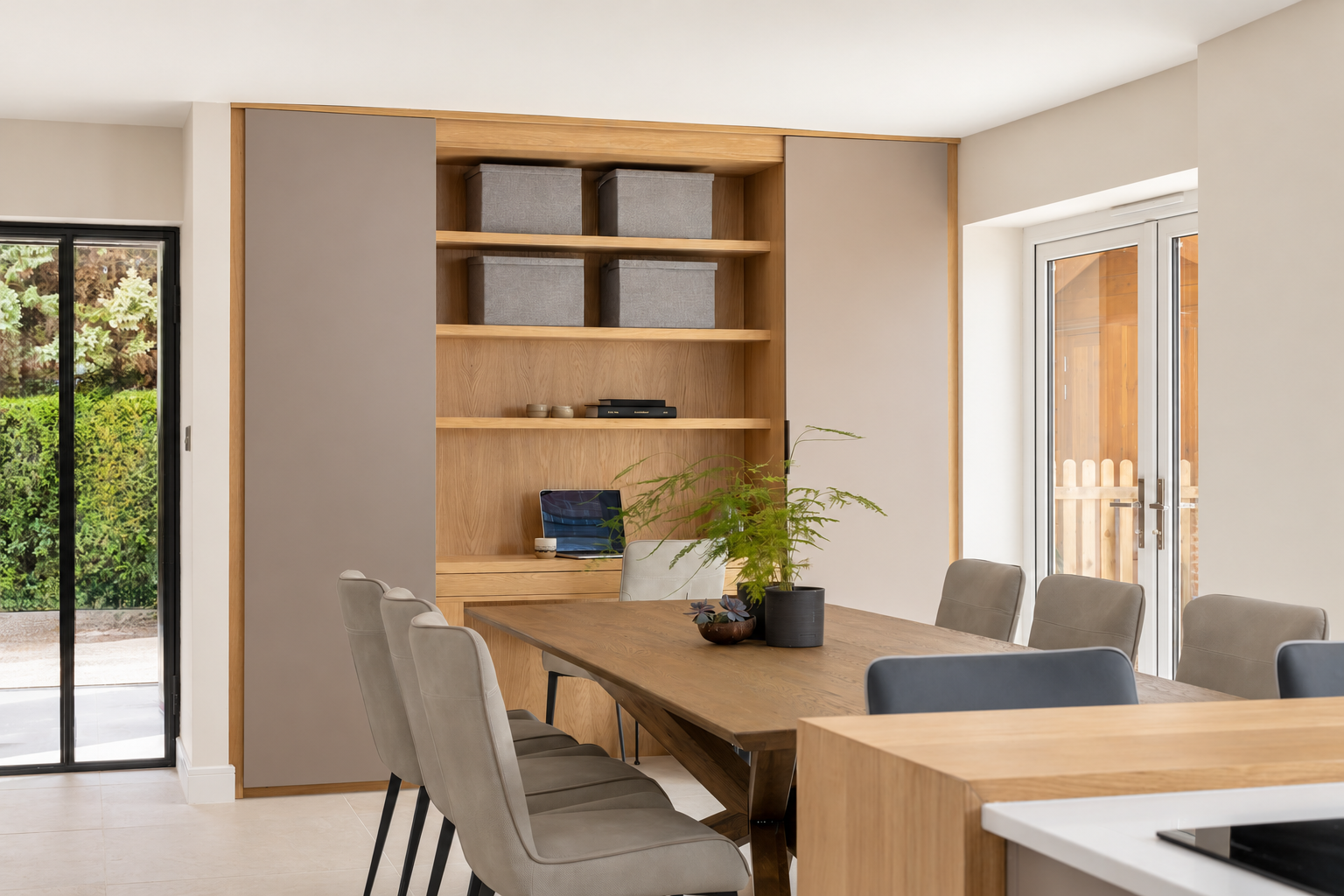 Oak dining table and upholstered chairs in front of a bespoke oak study with sliding doors at The Willows, Prestbury.